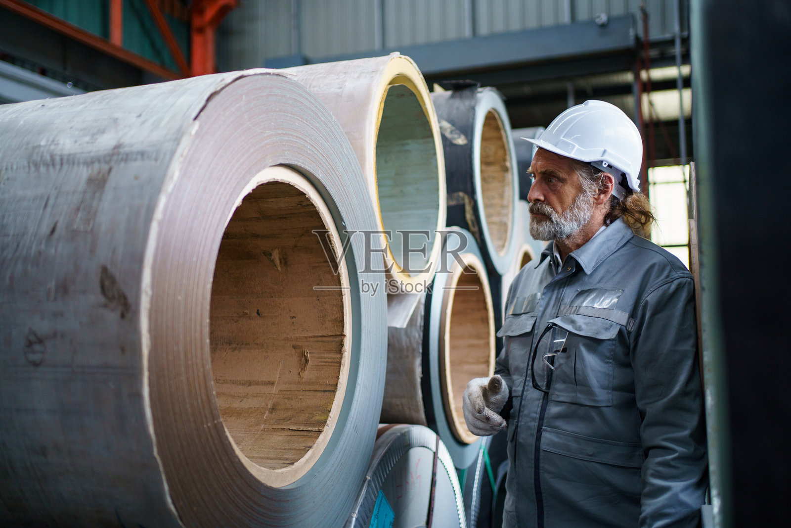 工厂里，一位资深工程师正在检查金属卷材，体现了质量控制的概念。照片摄影图片