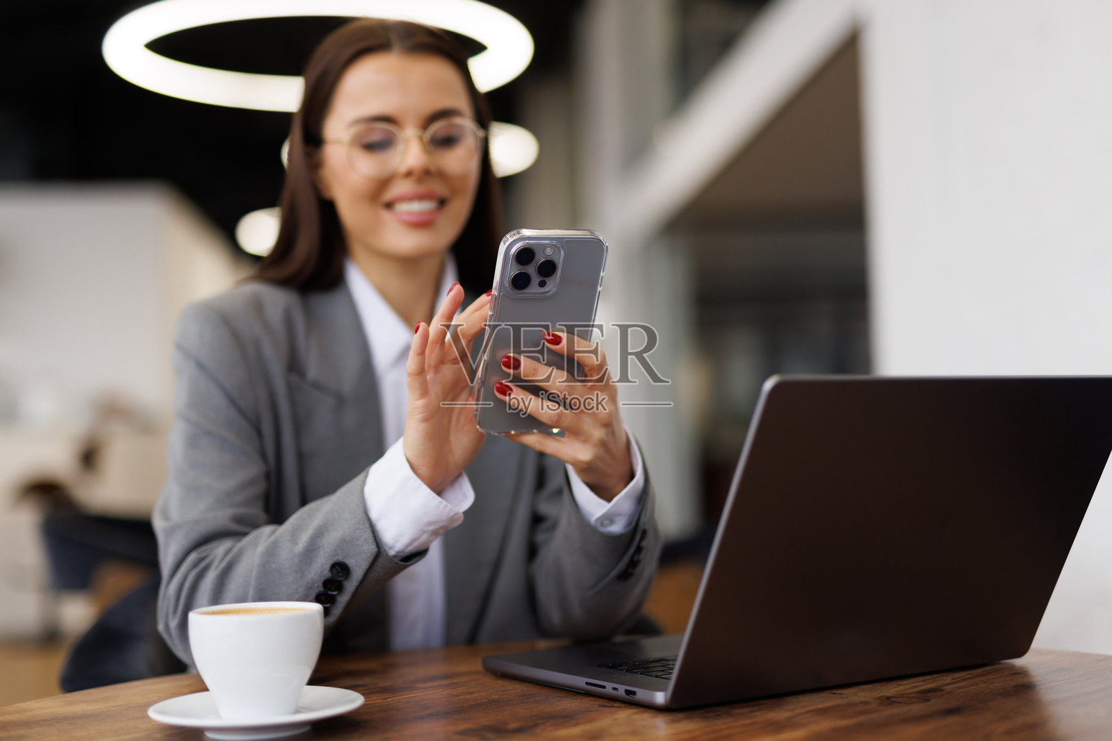 年轻女子坐在咖啡馆的木桌旁，喝着咖啡并使用智能手机。照片摄影图片