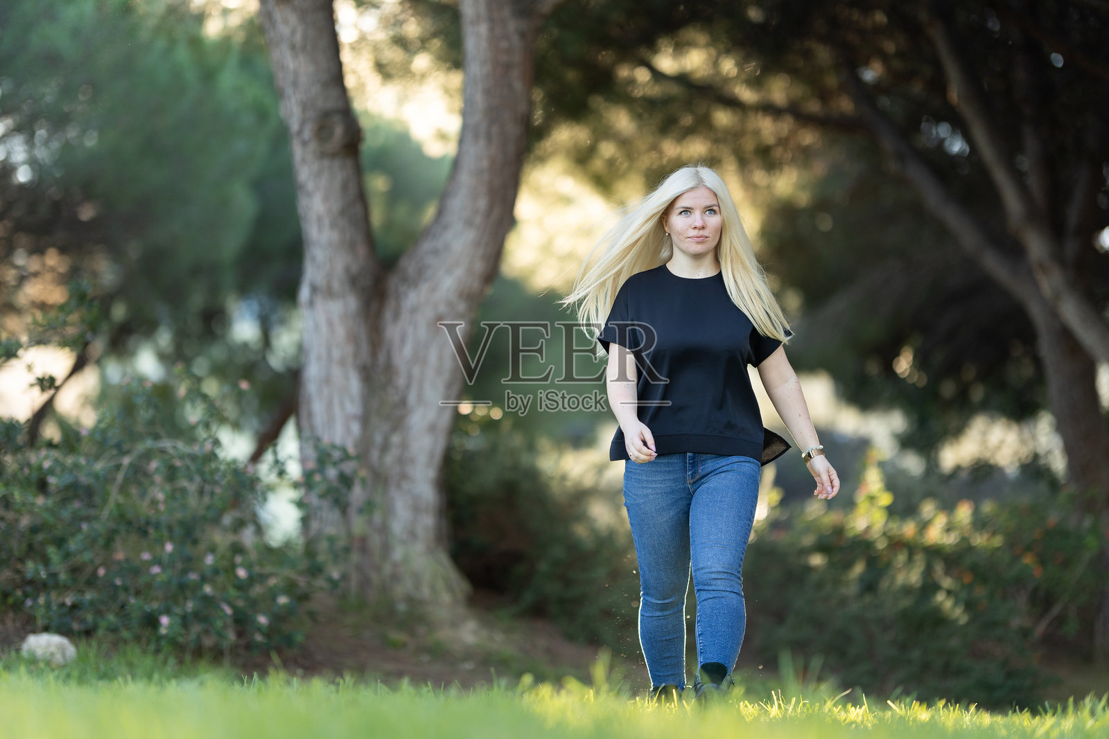 女人在公园里散步，周围有树木。照片摄影图片