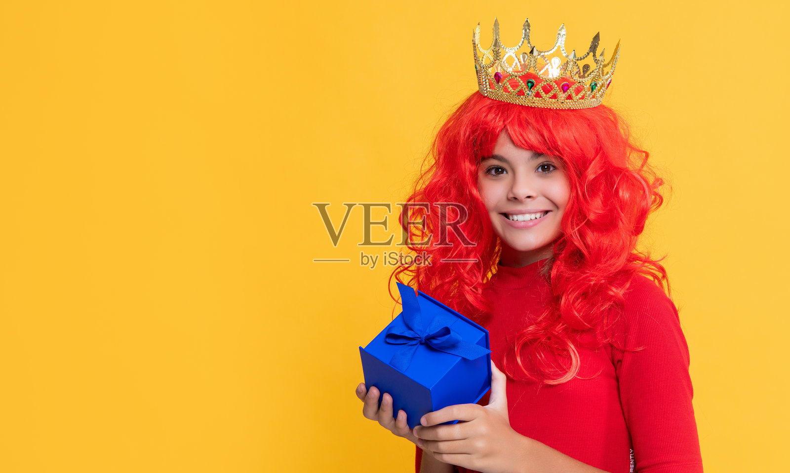 戴着皇冠的快乐女孩，背景为黄色，手持礼物盒照片摄影图片