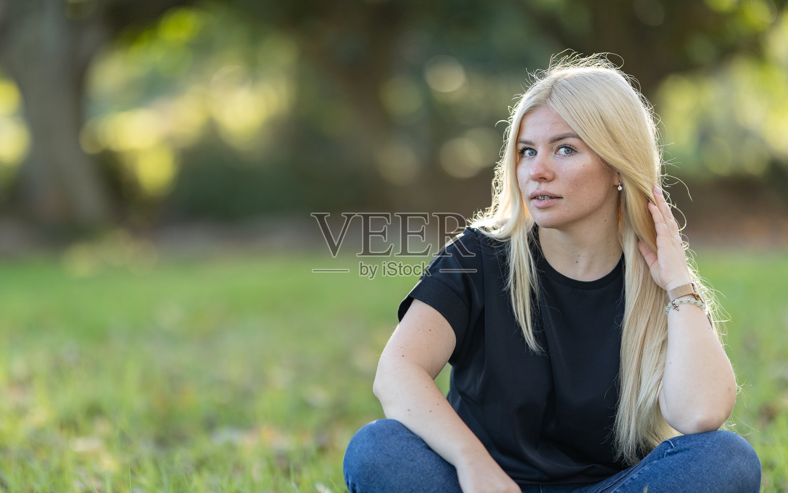 戴牙套的女人坐在草地上，一只手托着头照片摄影图片