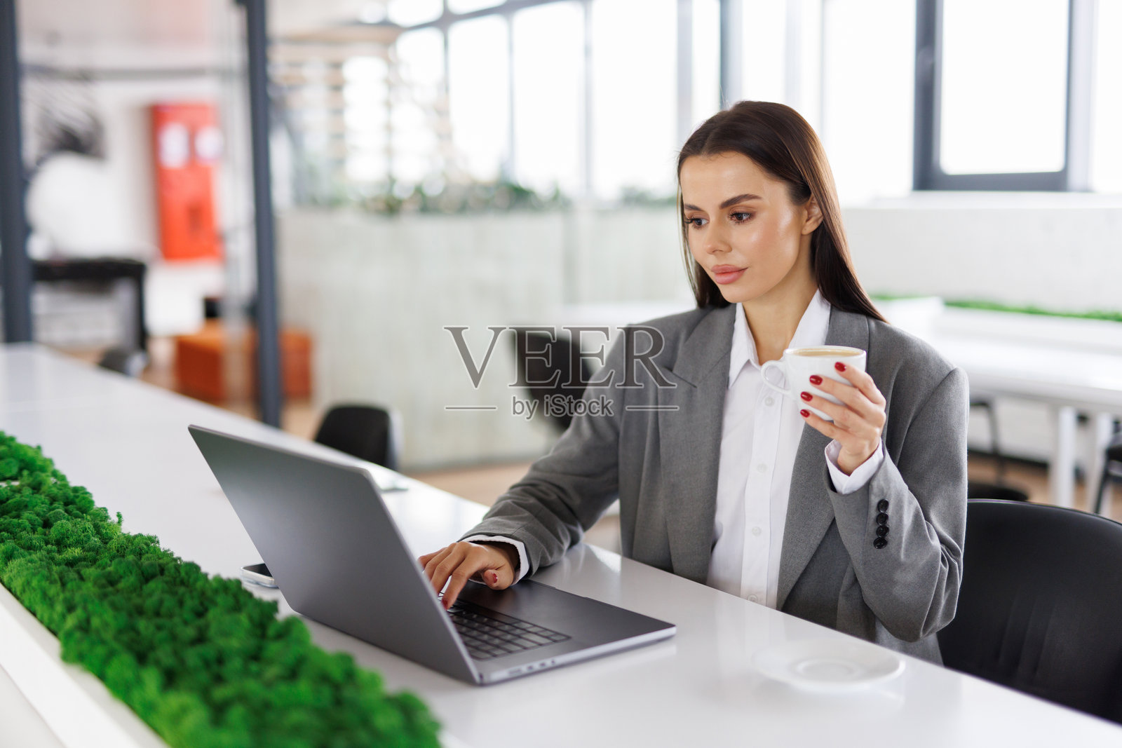 一杯好咖啡。年轻漂亮的女人坐在工作区，手里拿着咖啡杯。照片摄影图片