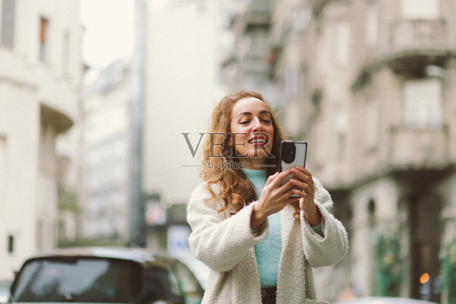 寒冷冬日，美丽的女子在城市街道上使用手机。照片摄影图片