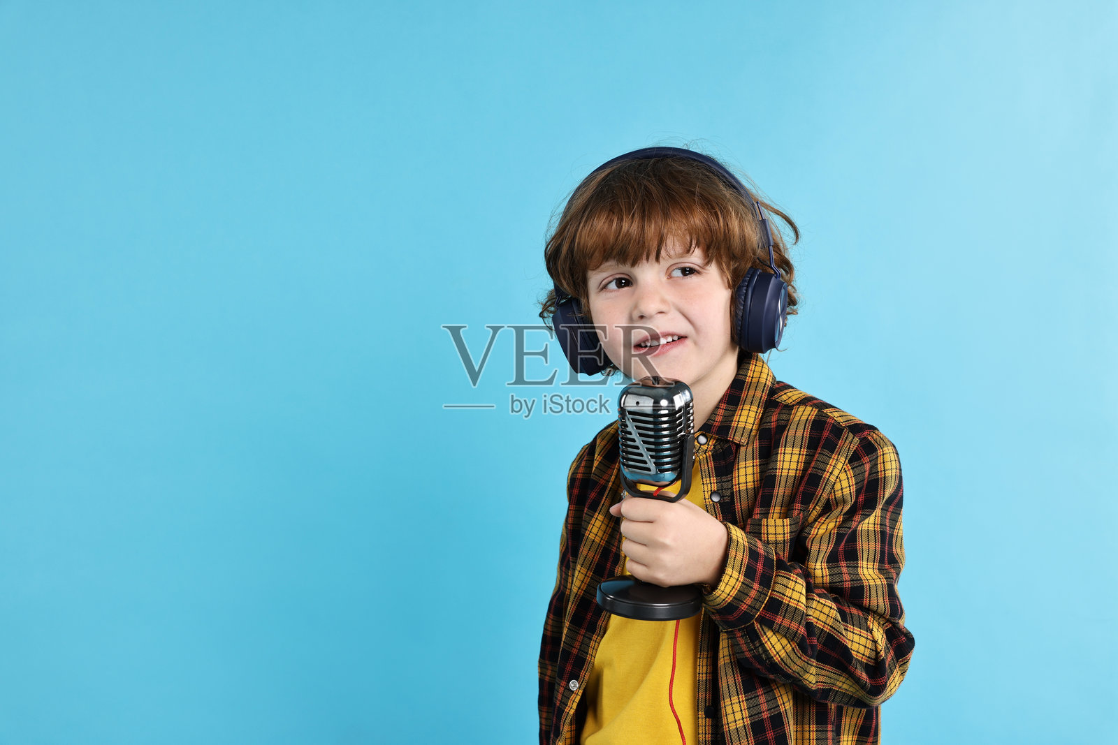 浅蓝色背景下，戴着麦克风和耳机的男孩，留有文字空间照片摄影图片