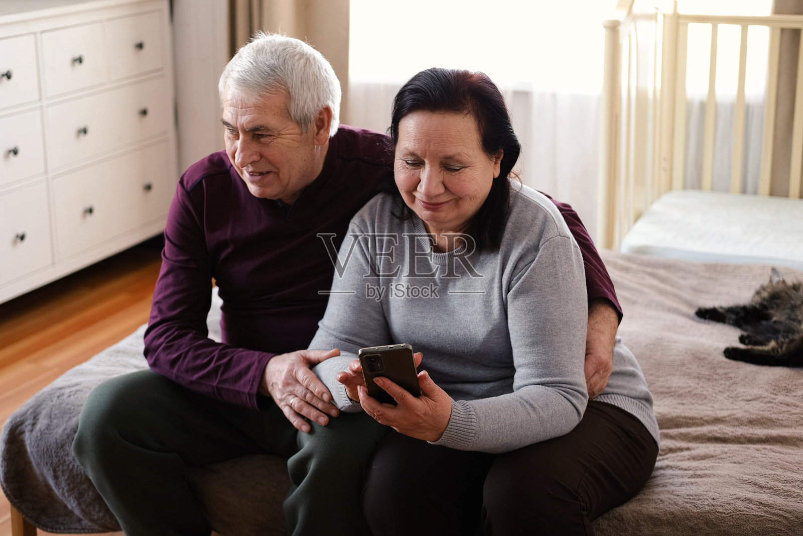 老夫妇在家中厨房放松时一起使用手机。年迈的男人和女人正用智能手机浏览网页，度过休闲时光。快乐的已婚老年夫妇正在打字、学习。照片摄影图片