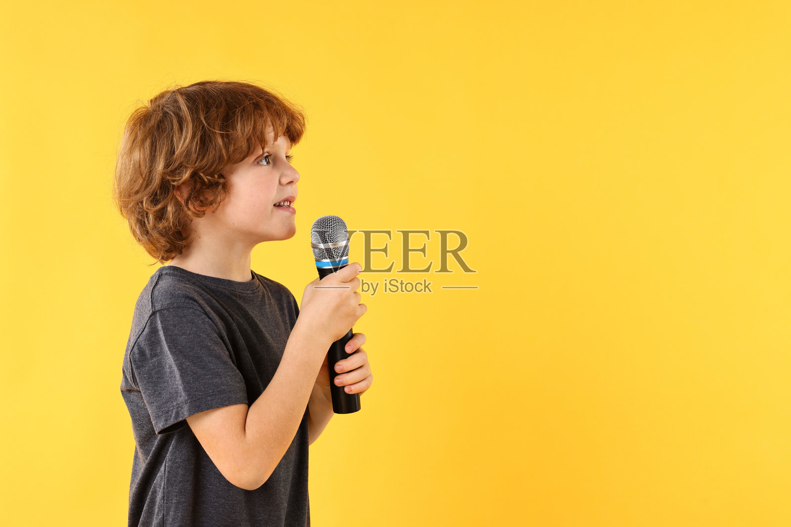 小男孩在黄色背景下拿着麦克风唱歌，有留白处可供添加文字照片摄影图片
