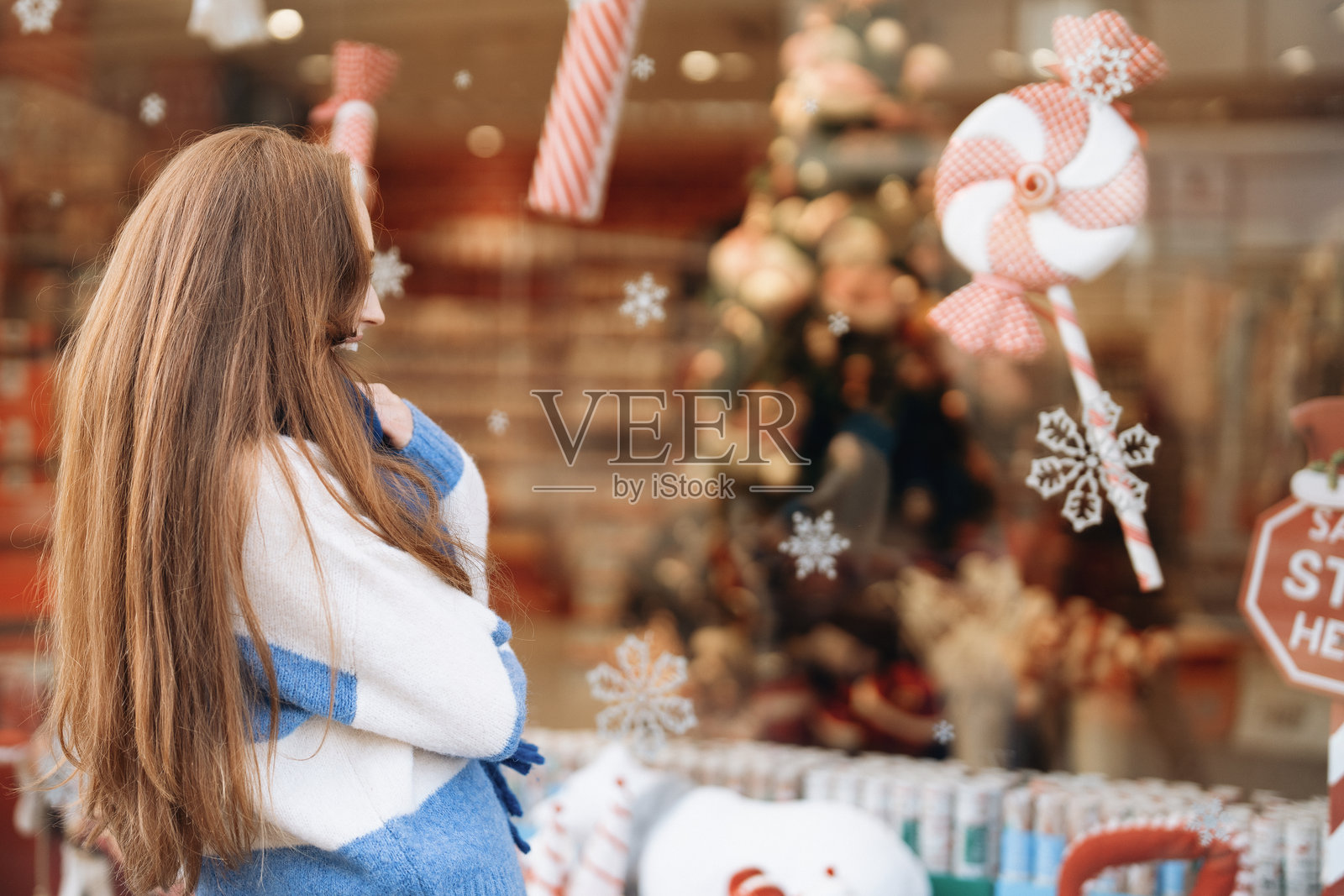 白天，一个女人正在看橱窗里展示的节日圣诞装饰。照片摄影图片