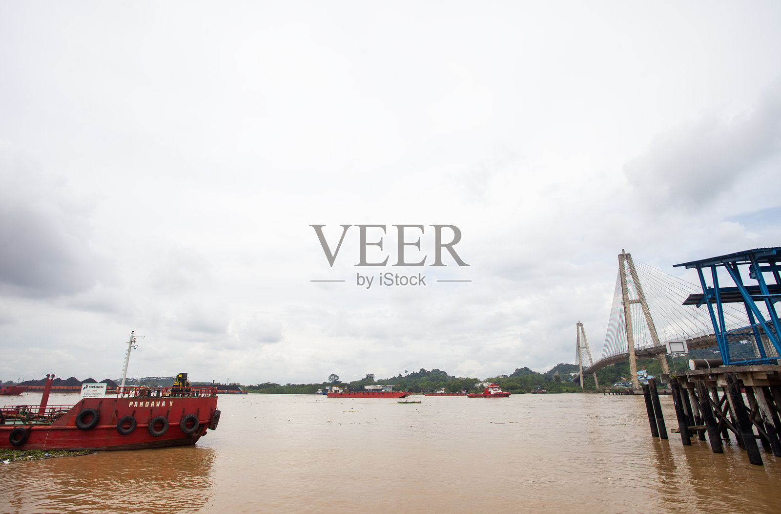 宏伟的马科塔二桥横跨婆罗洲三马林达的马哈坎河。一艘拖船在桥下拖曳着煤炭驳船，彰显了河流在工业运输中的重要作用。照片摄影图片