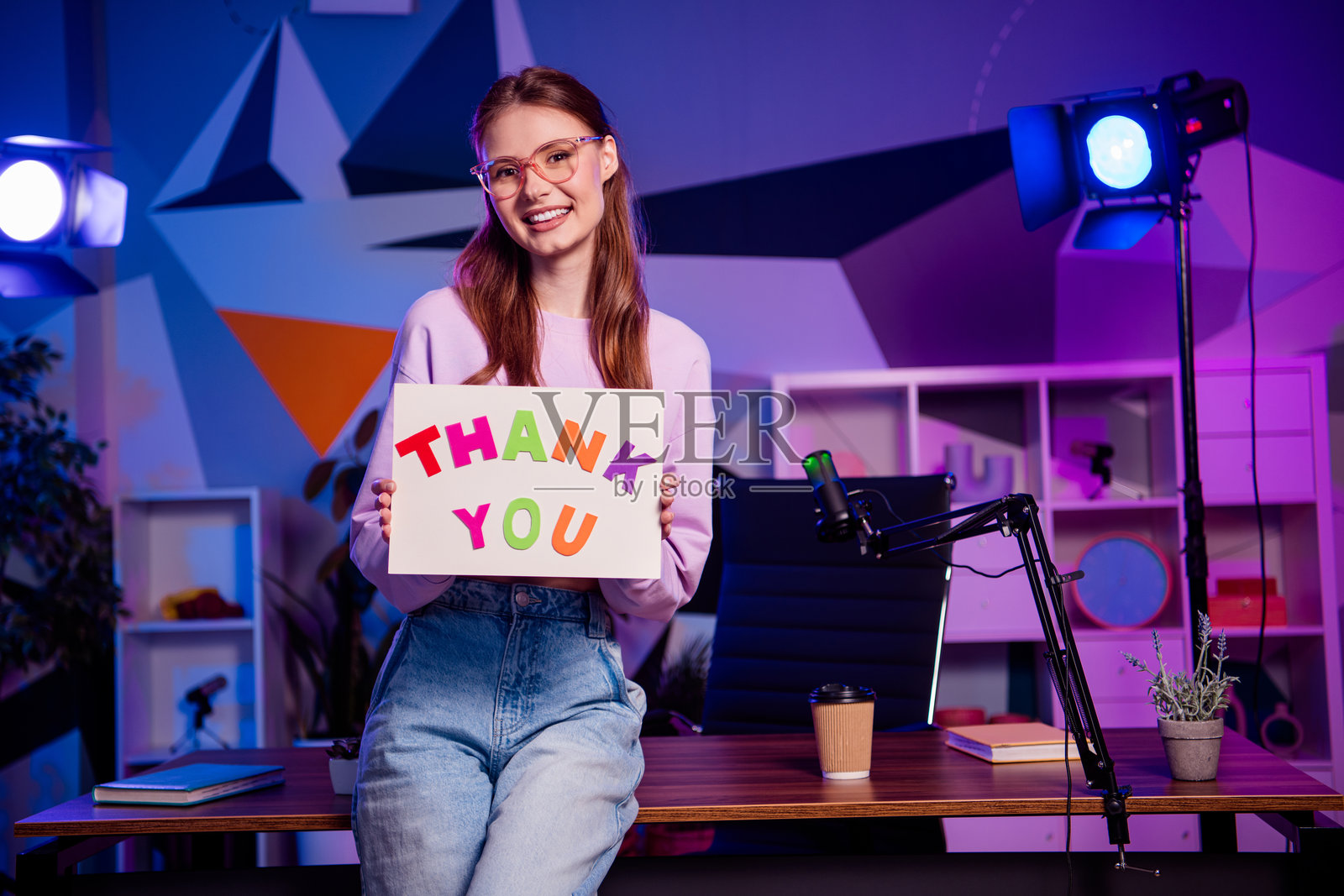 年轻的女博主在色彩缤纷的录音棚里举着感谢牌，旁边放着麦克风，用于媒体和广播内容创作。照片摄影图片