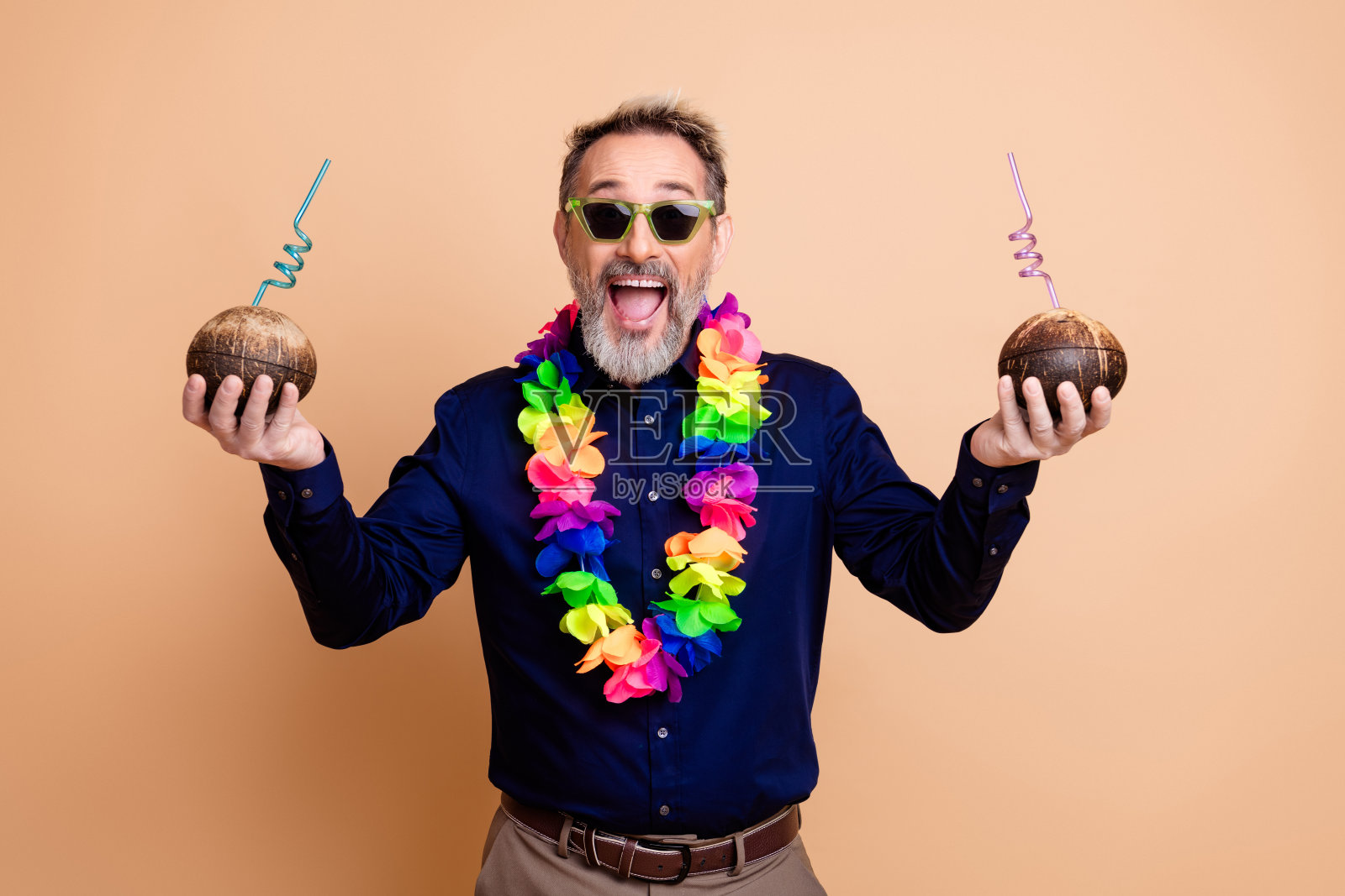 身着正装、戴着彩色花环的快乐商人，手持插着吸管的椰子，背景为米色。照片摄影图片