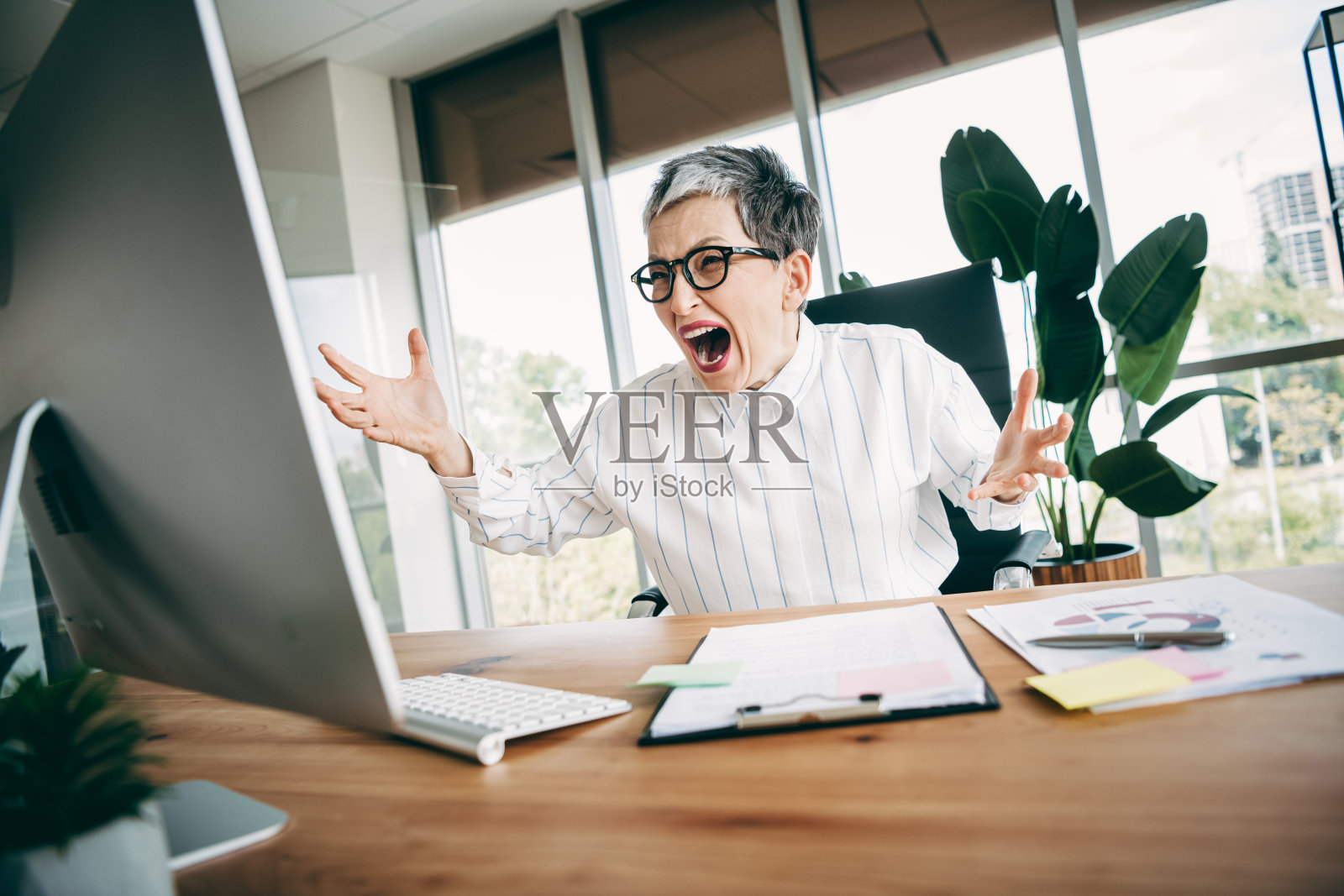 忙碌的职业女性在现代办公室工作区内，周围有办公用品和电脑，表达着沮丧的情绪。照片摄影图片