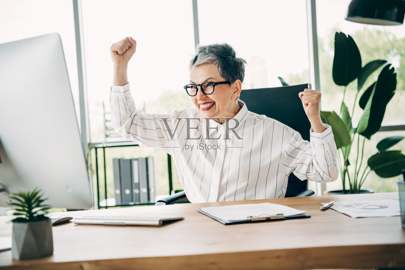 一位专业的女商人正在现代工作空间庆祝成功，脸上洋溢着快乐和自信。照片摄影图片