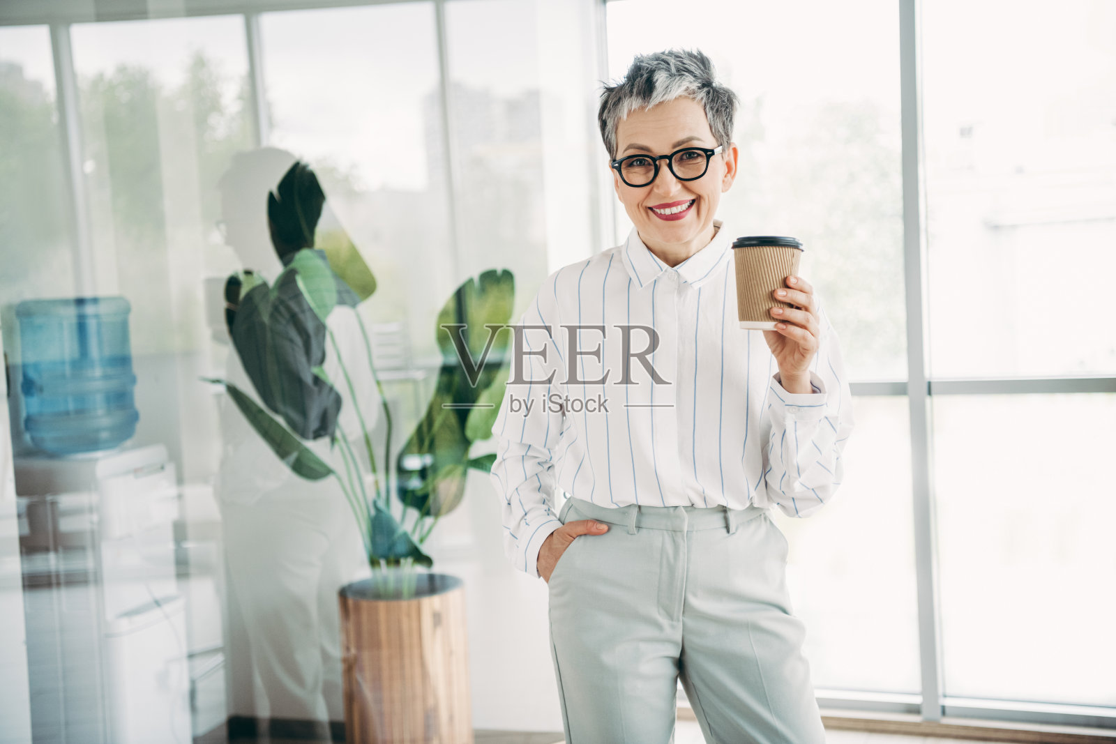 自信的女商人站在现代办公室，手持咖啡，象征着在企业界的成功和专业精神。照片摄影图片