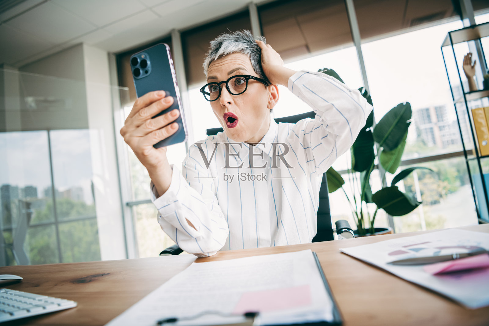 现代办公室里，一位职业女性被手机屏幕上的内容惊艳，办公室采光良好，氛围专业。照片摄影图片