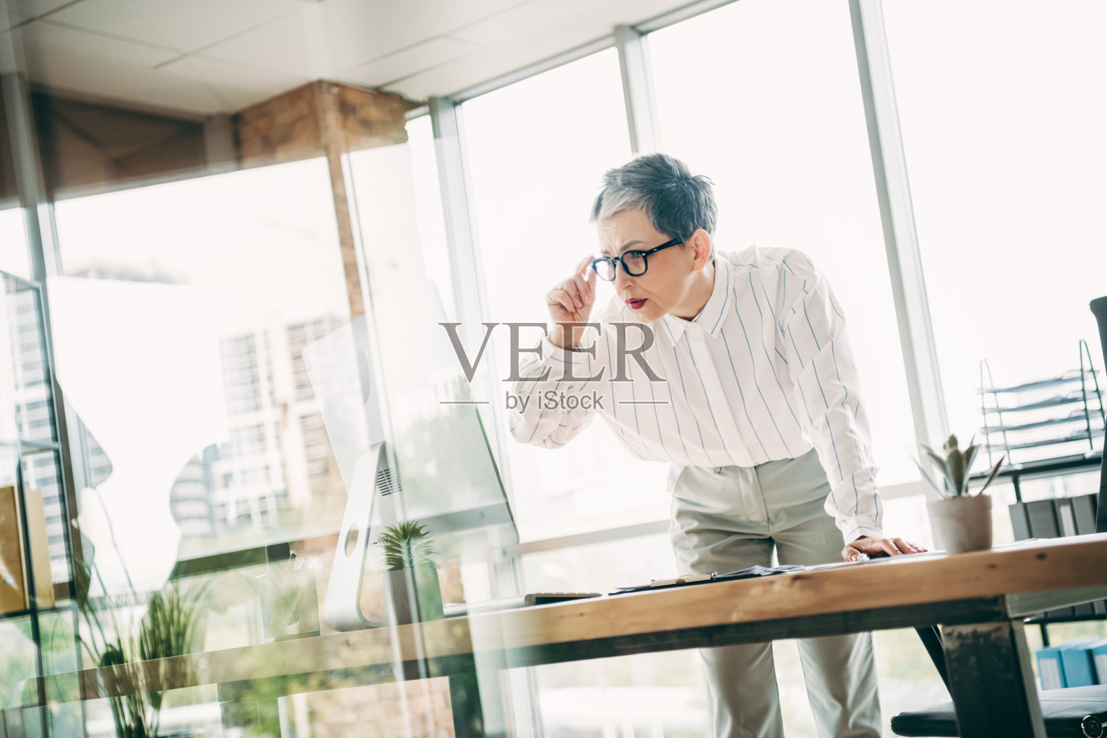 一位成熟的职业女性在现代室内办公室工作区，在电脑前分析数据照片摄影图片