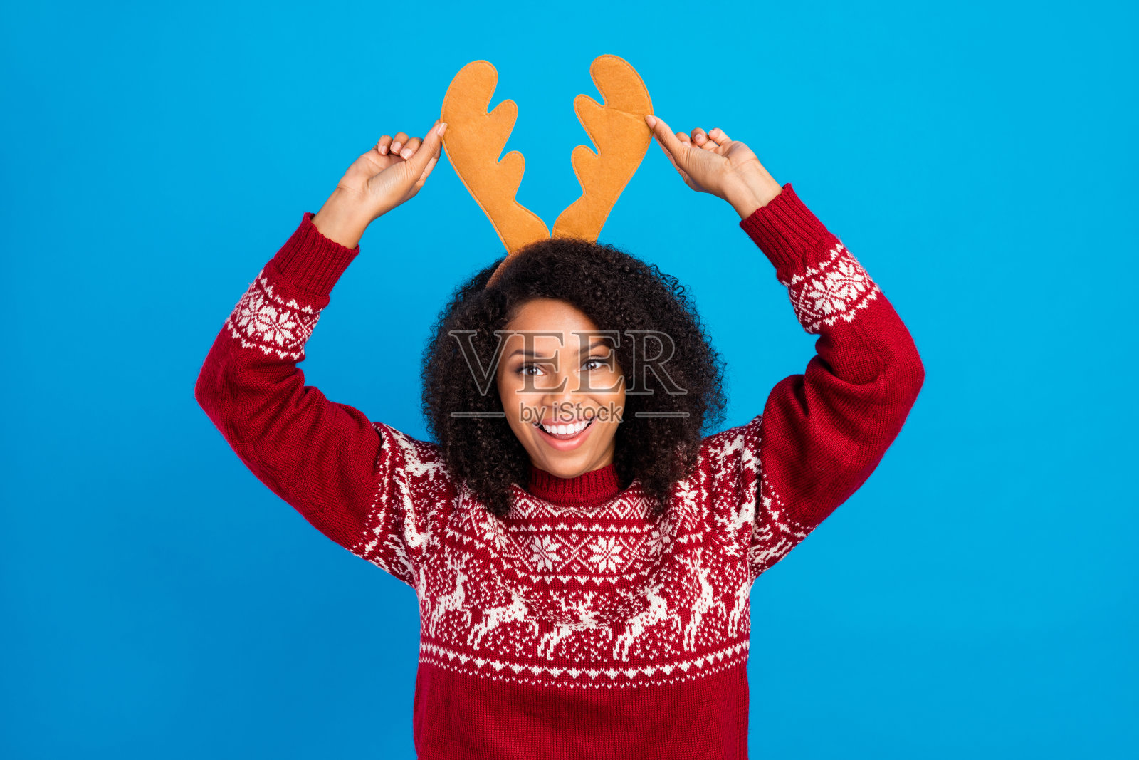 年轻快乐的黑人女孩，面带喜悦的笑容，双手触摸鹿角，孤立在蓝色背景上。照片摄影图片