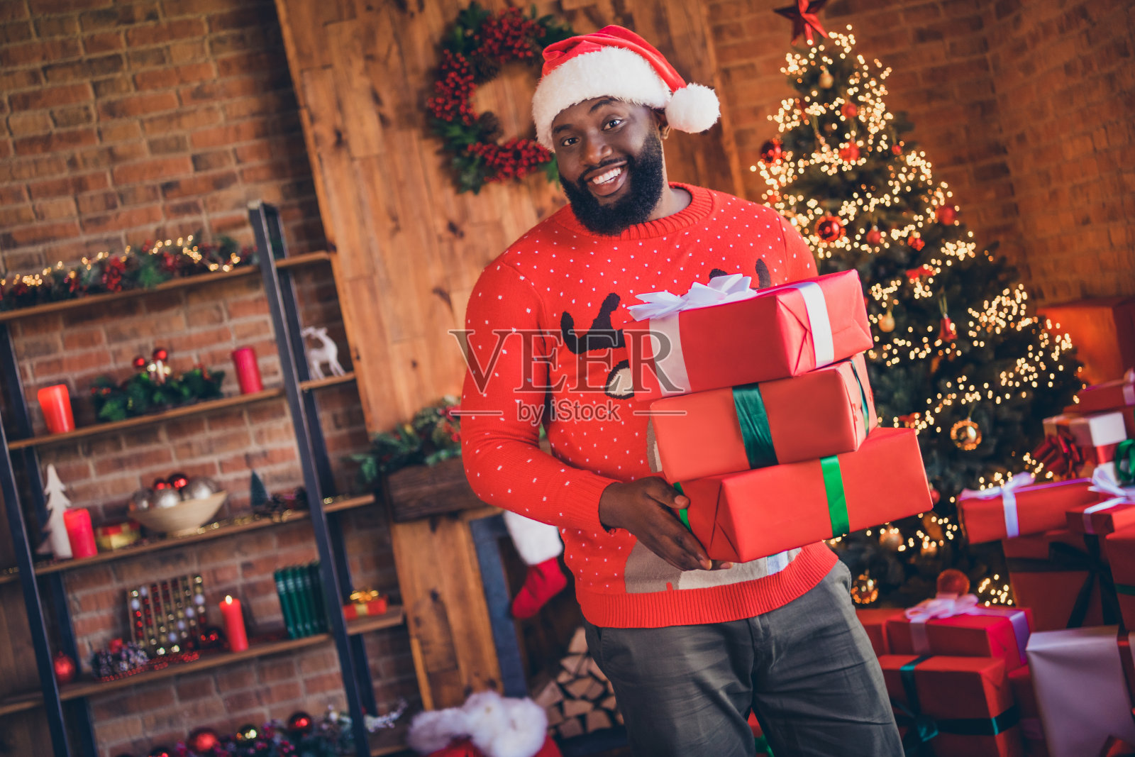 照片：一个开心的非裔美国年轻男子在室内家中拿着礼品盒，庆祝圣诞节。照片摄影图片