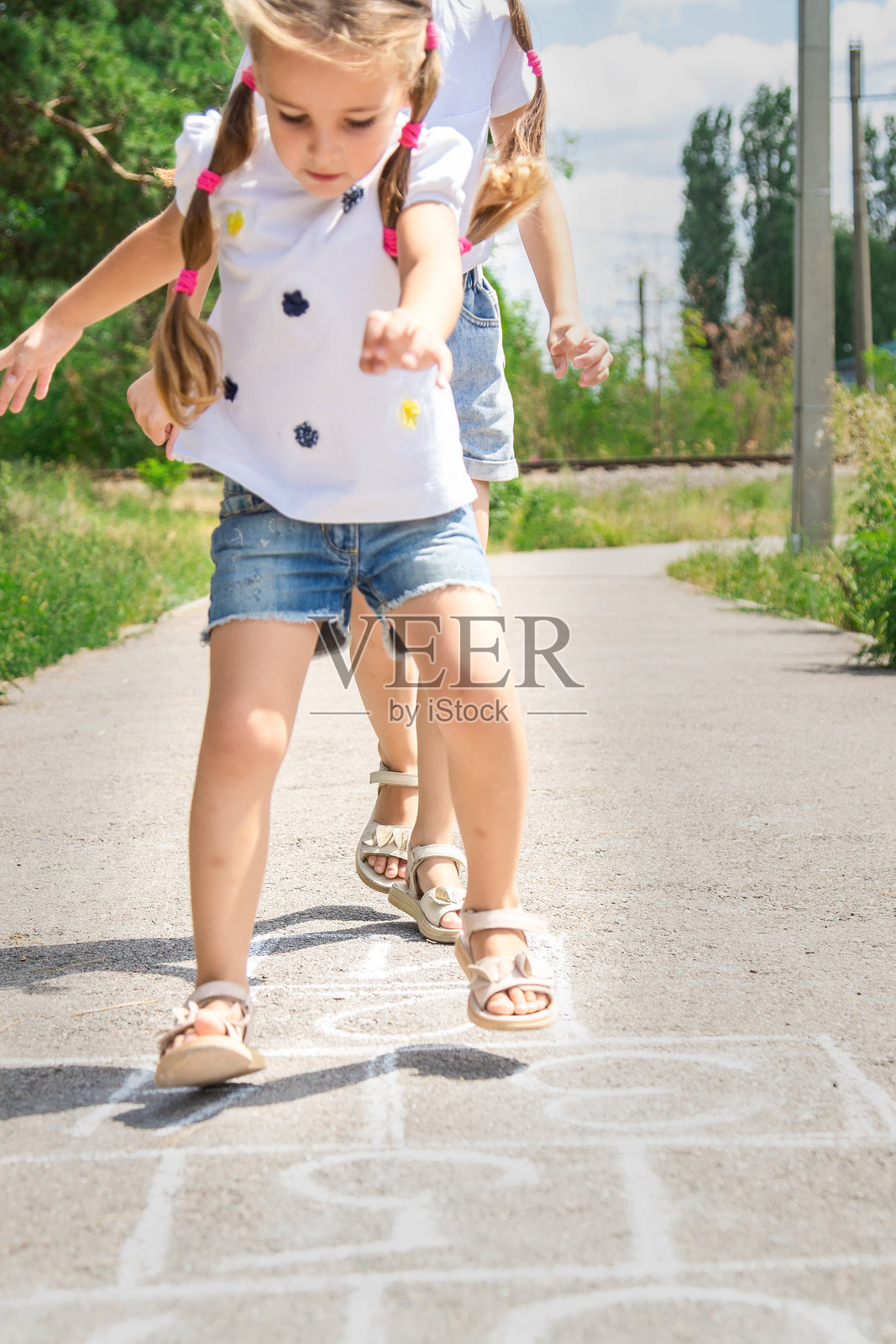 女孩在户外游乐场和姐姐玩跳房子，孩子在户外玩耍。小孩在人行道上画的跳房子。户外的儿童活动。照片摄影图片