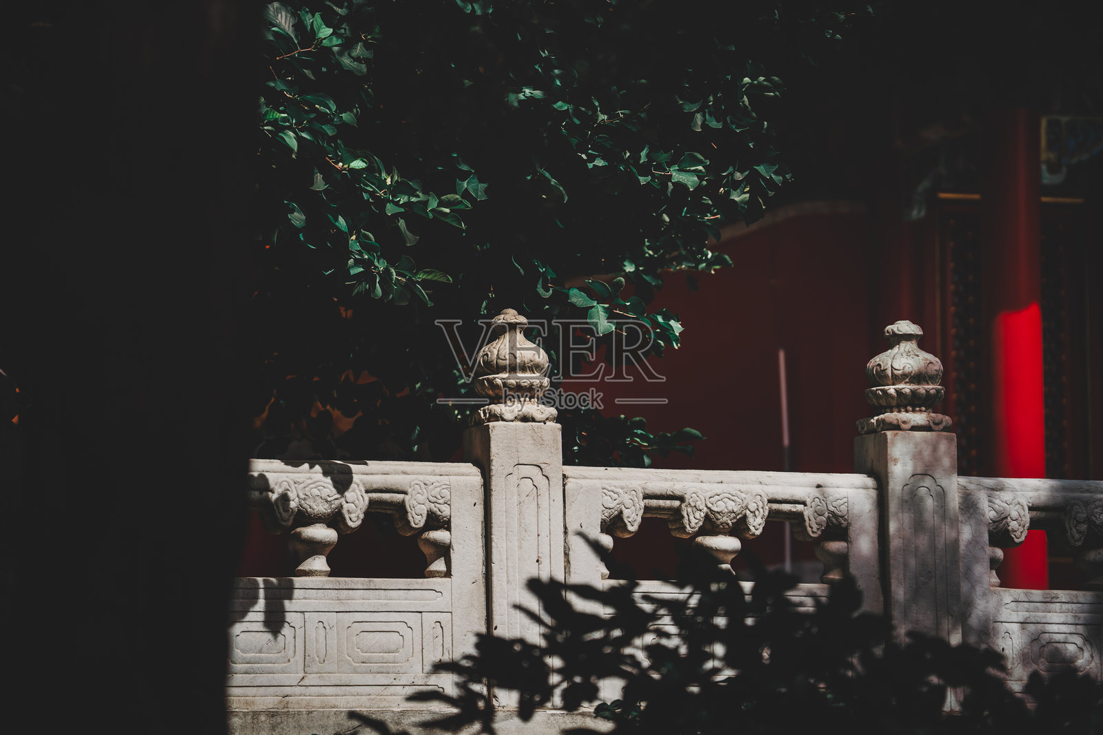 北京故宫的宁静景观。石栏上的植物围绕着沐浴在阳光下的红墙。光影交错。这张图片体现了经典的建筑风格。照片摄影图片