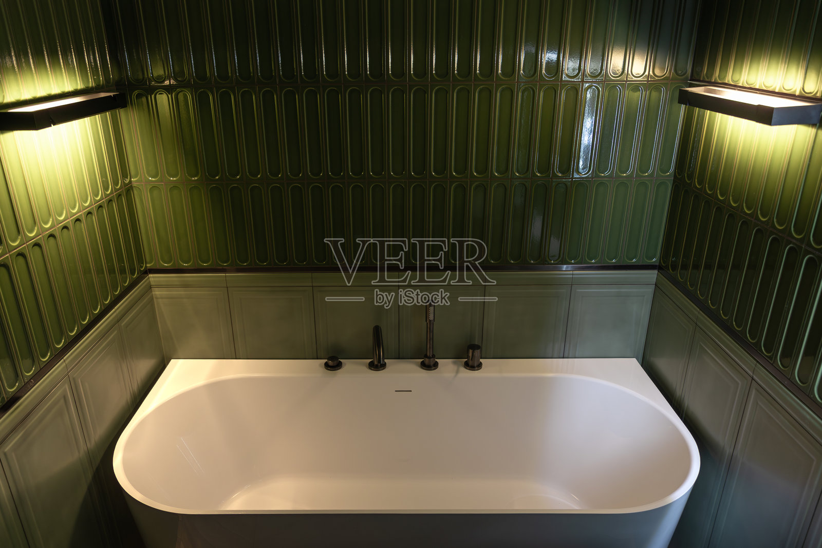 深色卫浴配件的浴缸，搭配绿色瓷砖和柔和的光线，营造夜晚的放松氛围。照片摄影图片