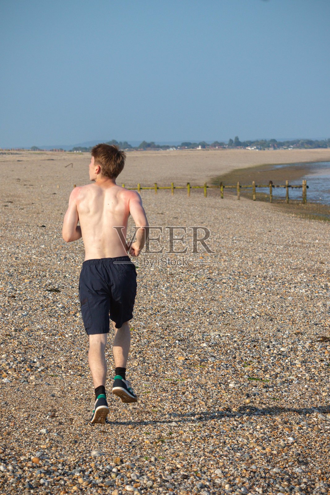 一个少年在海滩上跑步离去，上半身赤裸照片摄影图片