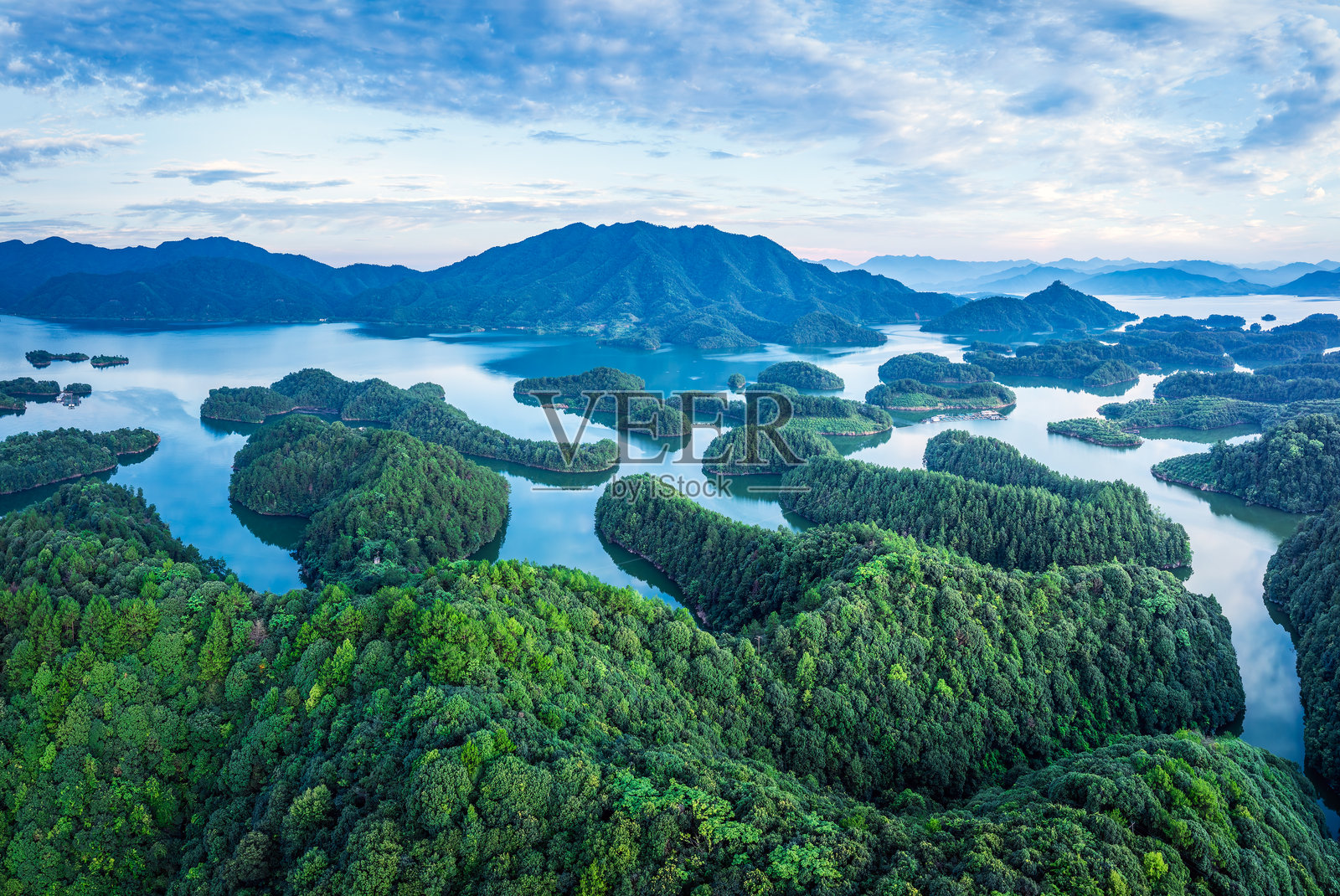 日出时分，群山环绕的宁静湖面上散落着无数翠绿的岛屿，俯瞰视角。照片摄影图片