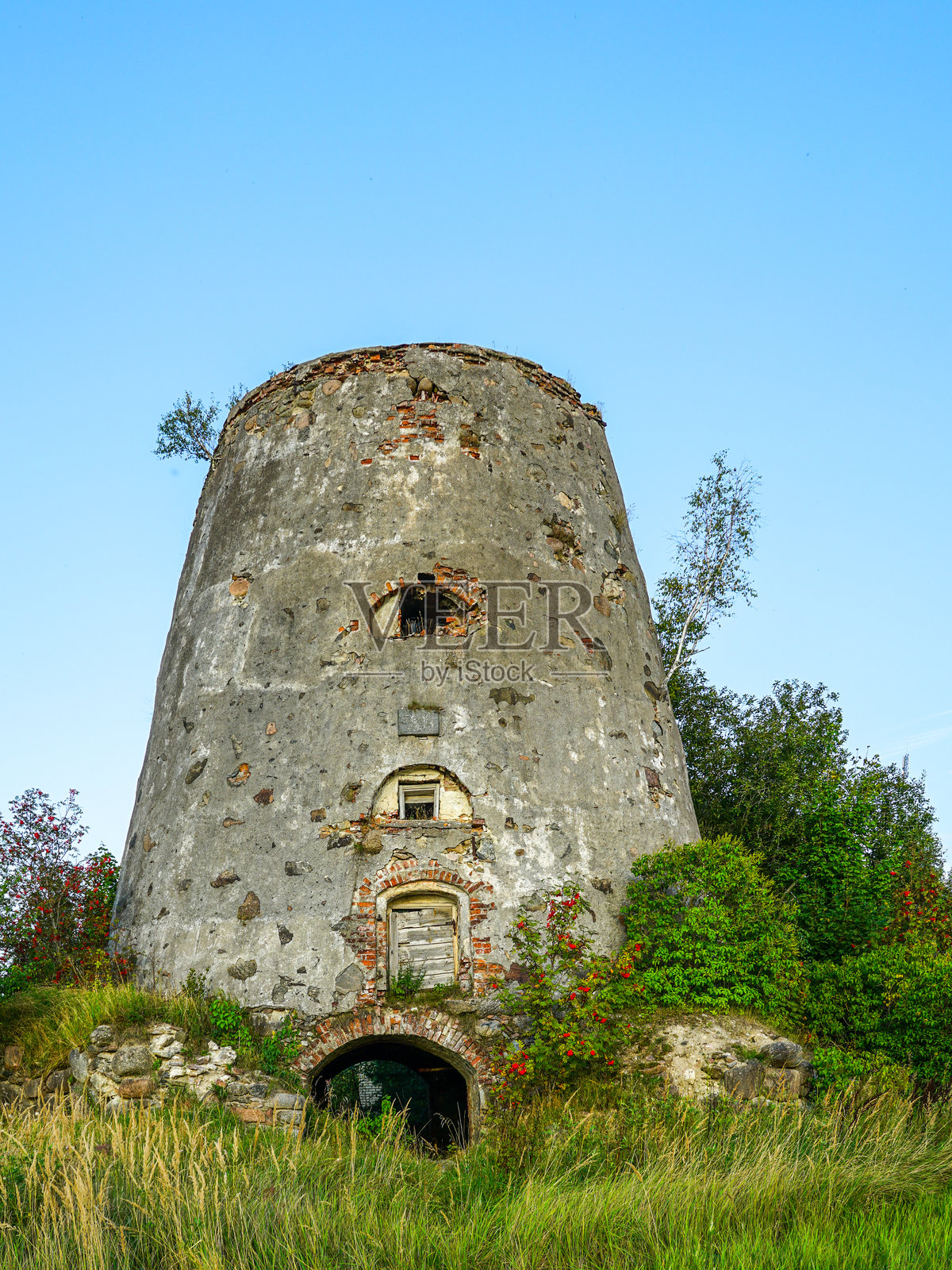 夏日里，被草地和绿植环绕的废弃历史石头风车塔，带有砖砌细节。照片摄影图片