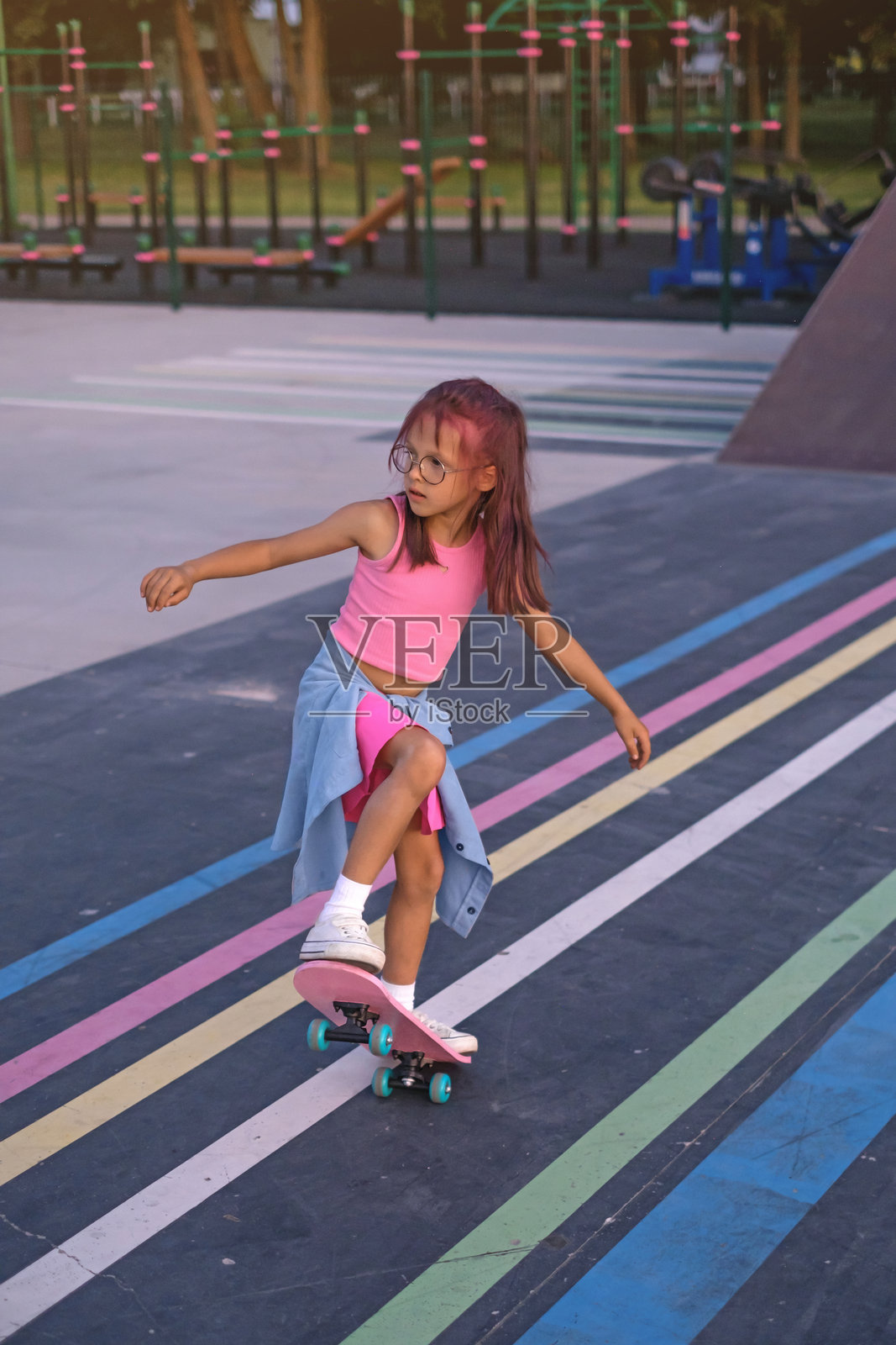 一个时髦的小女孩，正在玩滑板，摆出做动作的姿势。照片摄影图片