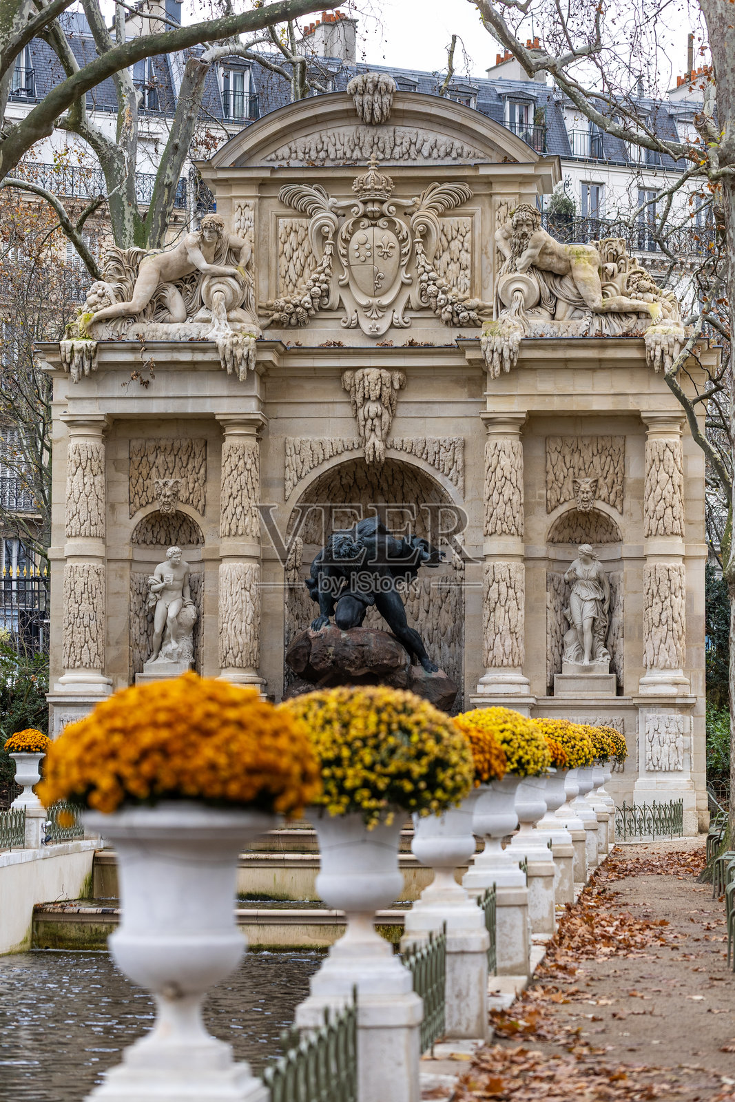 法国巴黎卢森堡公园的美第奇喷泉，配有华丽的雕塑和菊花花瓶。阴天时，地上有光秃的树木和落叶。照片摄影图片