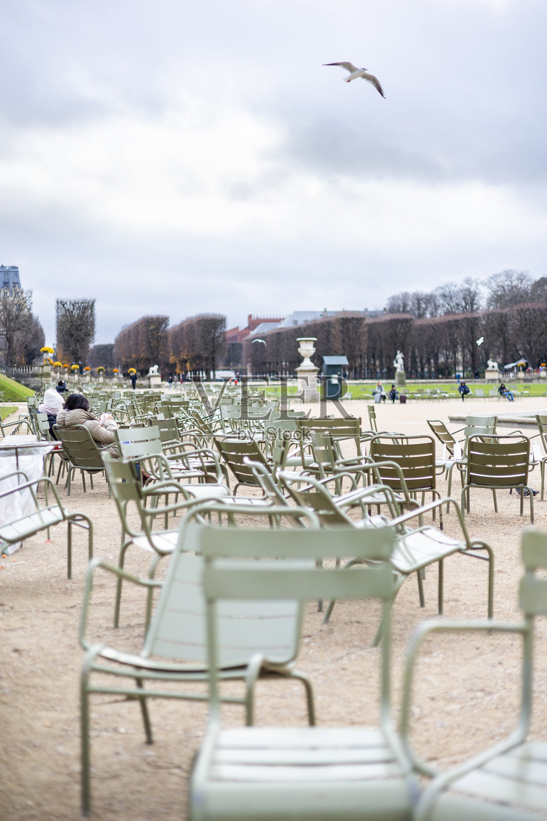 法国巴黎卢森堡公园里，一条碎石小径上摆放着几把浅绿色的金属椅子。阴天的秋日背景中可以看到一些辨认不出身份的人。照片摄影图片