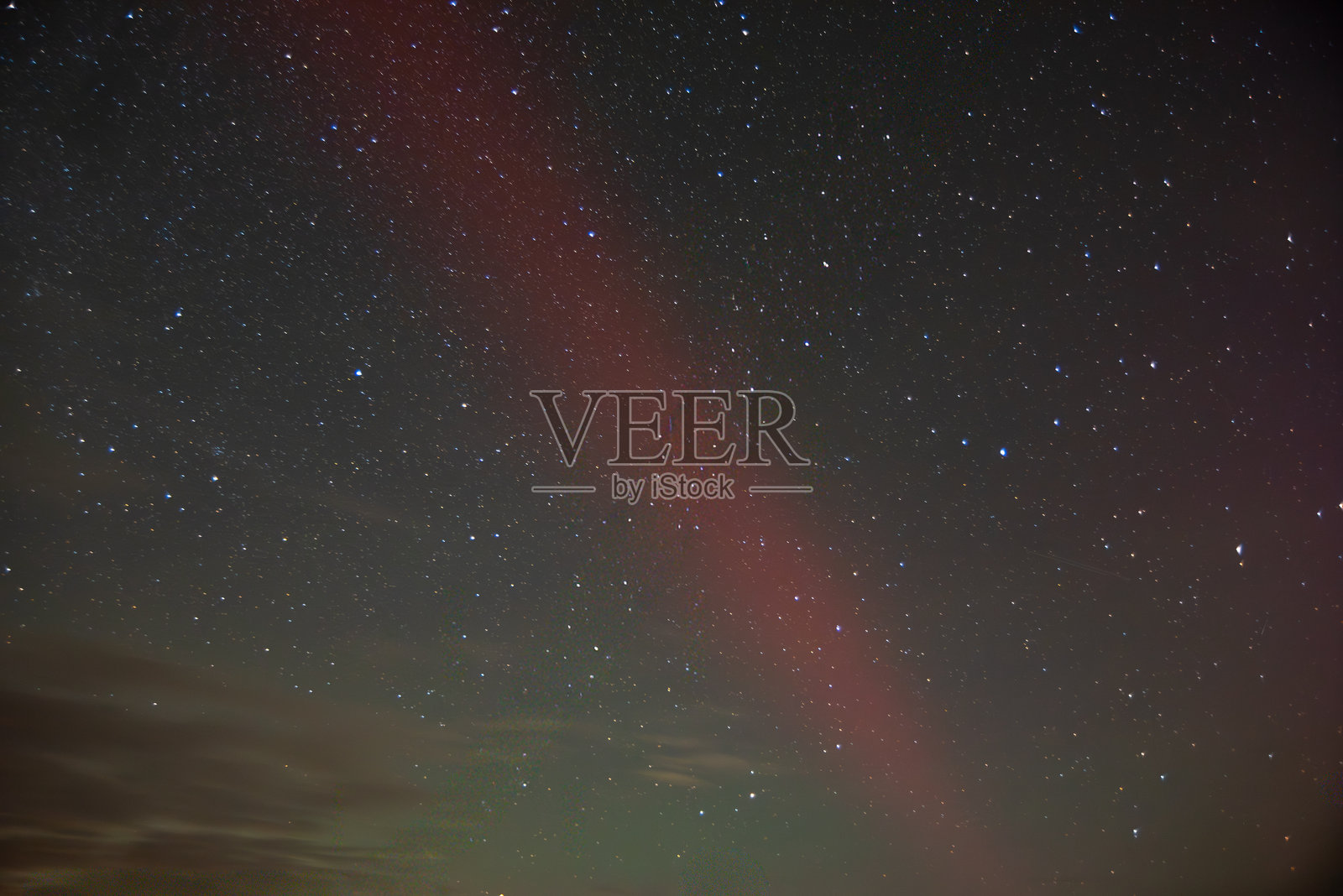 星空，一道微弱的红色极光划破黑暗，周围是无数可见的星星和淡淡的云彩。照片摄影图片