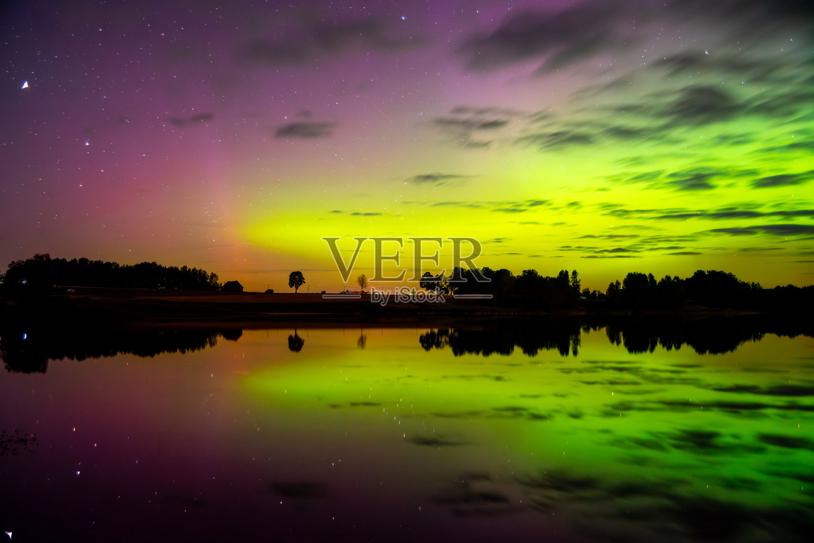 夜空中，绚丽的绿色和紫色极光闪耀，在平静的湖面上投下完美的倒影，湖边点缀着剪影般的树木。照片摄影图片