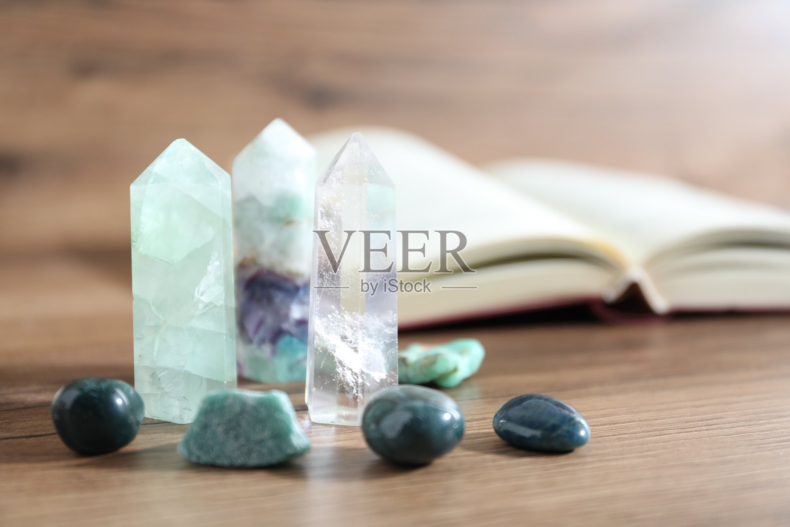 木桌上摆放着不同的疗愈石和一本书，特写镜头。照片摄影图片