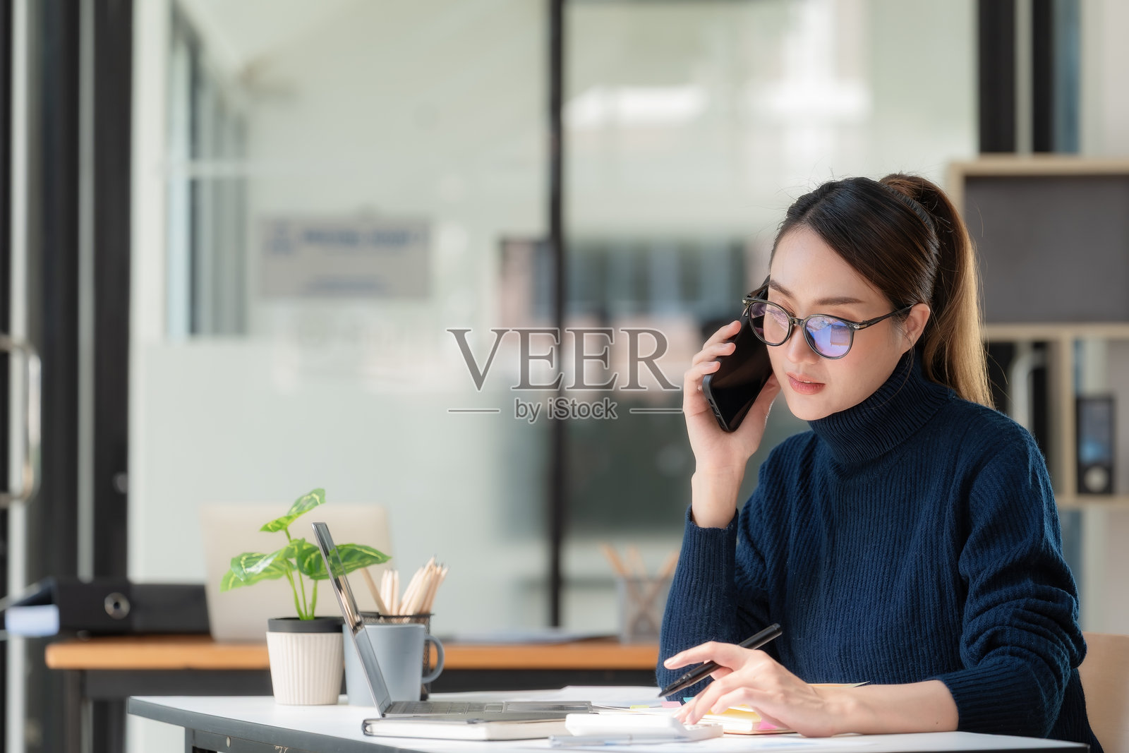 一位亚洲女商人正在办公室里与她的商业伙伴通电话，洽谈一笔生意。照片摄影图片