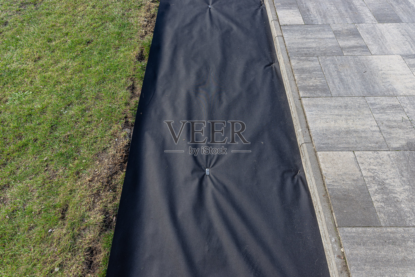 在花园里铺设厚厚的农用纺织品，可以看到篱笆和草坪。照片摄影图片