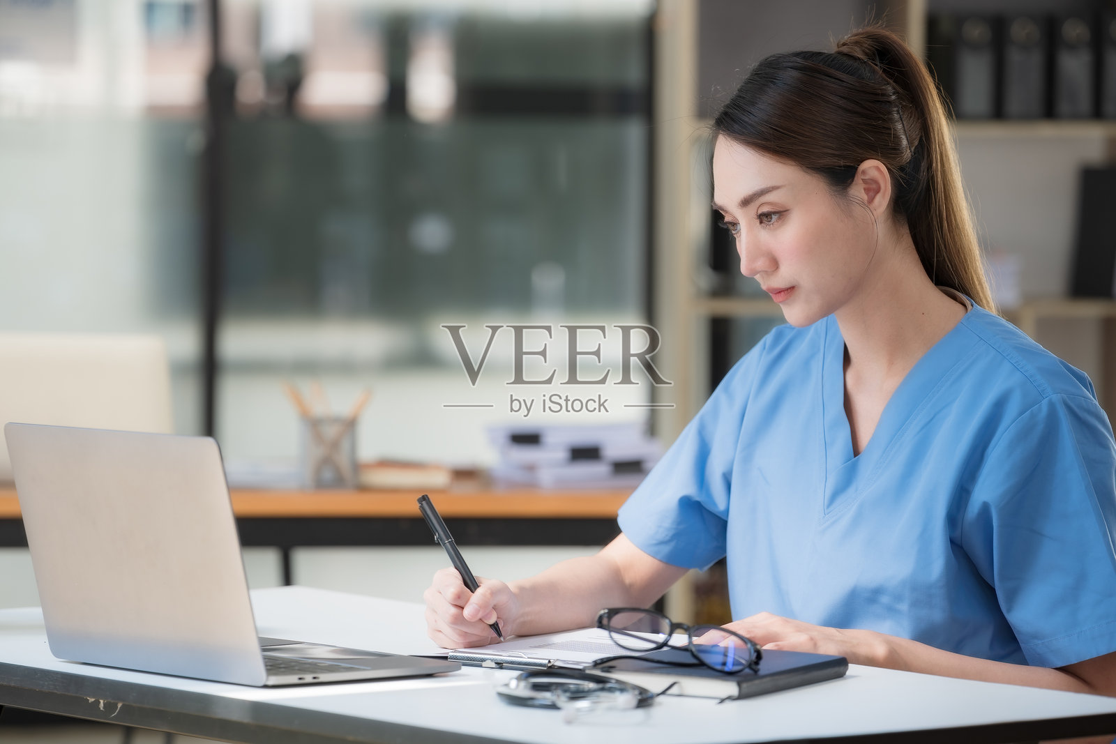 一位身穿蓝色外套的美丽亚洲女医生正在看笔记本电脑。照片摄影图片