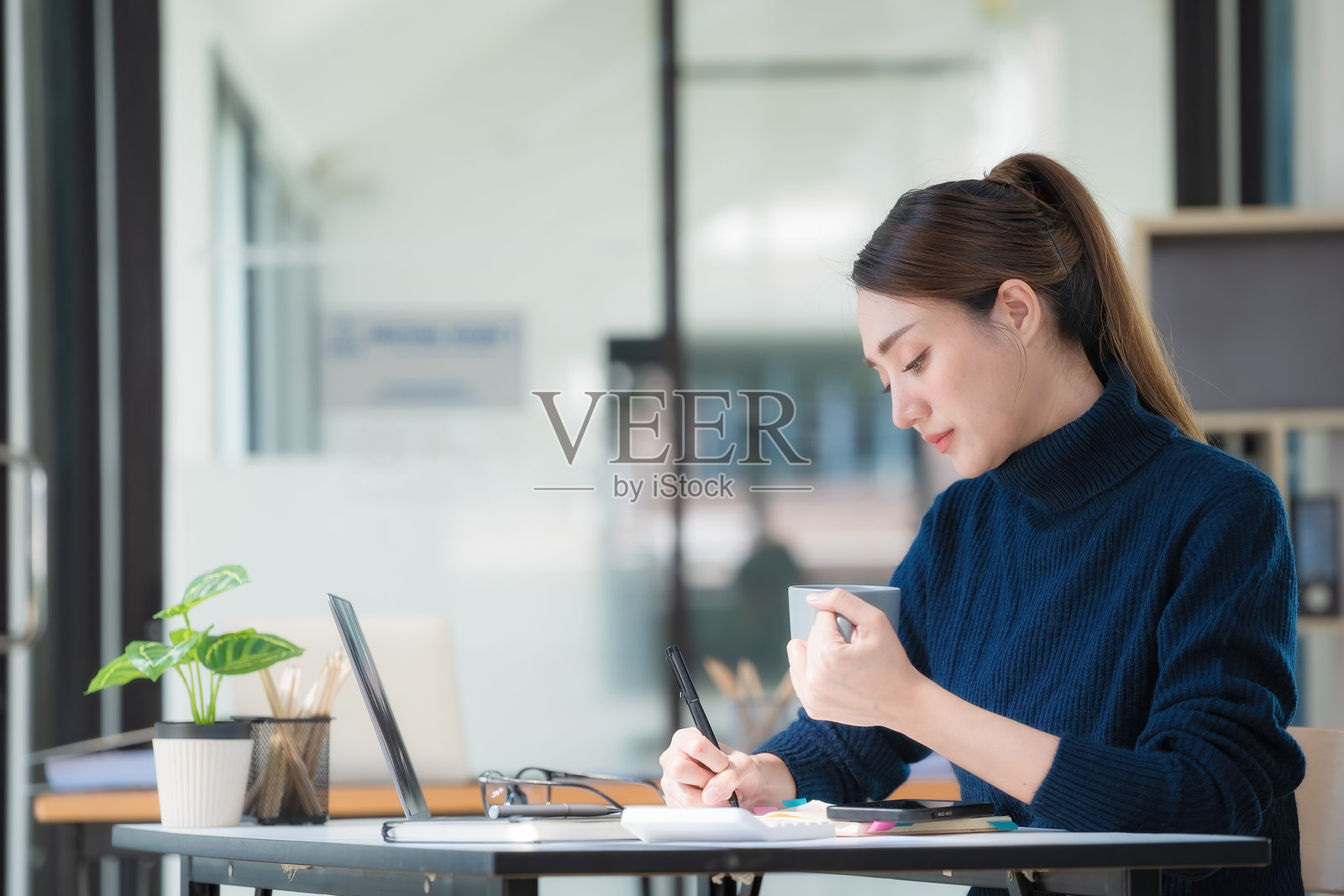 一位亚洲女商人一边使用笔记本电脑一边拿着一杯热咖啡。照片摄影图片