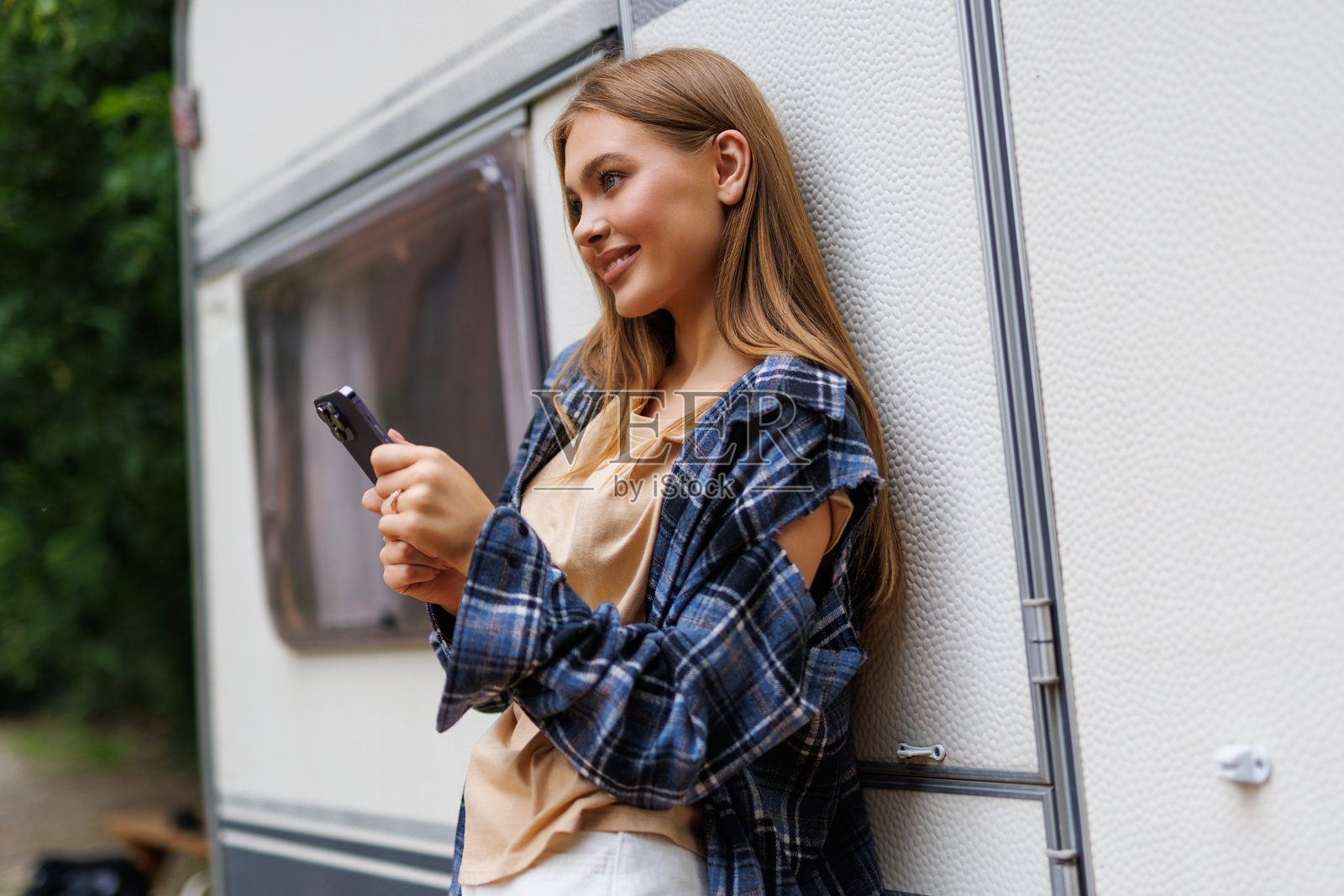 快乐的女人在乡村露营旅行中，站在露营车旁使用智能手机，有复制空间。照片摄影图片