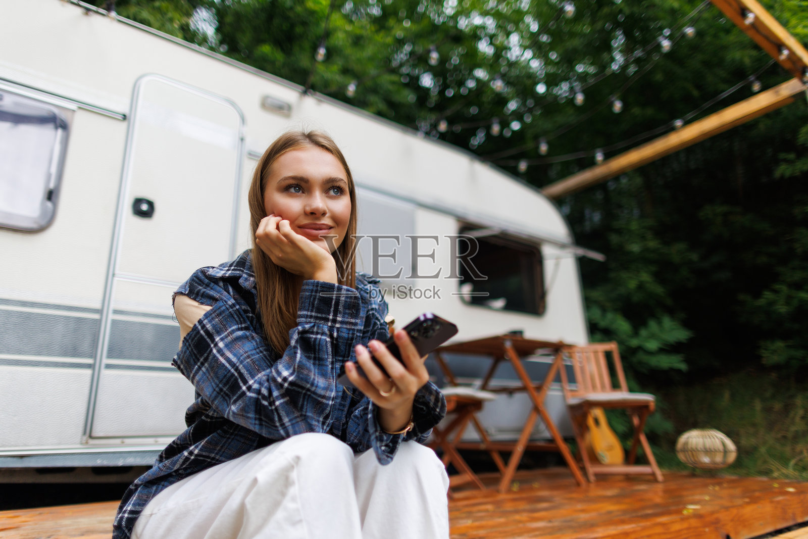 快乐的年轻女子在营地使用手机，背景有拖车照片摄影图片