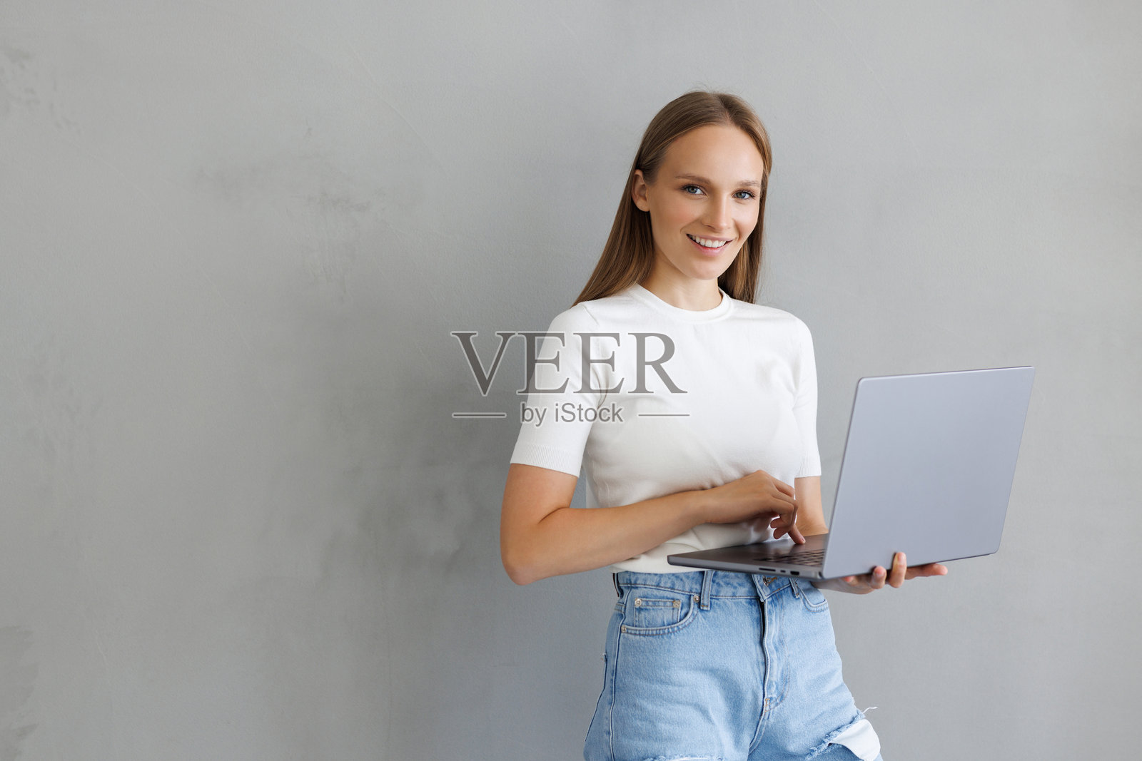 年轻女子身着休闲装，手持笔记本电脑，正给最好的朋友发邮件。照片摄影图片