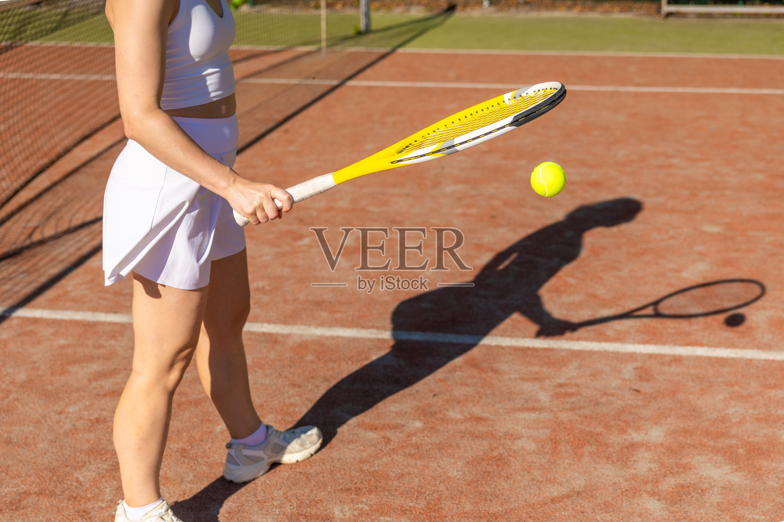 阳光明媚的练习日，特写网球拍、网球和在红土球场上的影子照片摄影图片