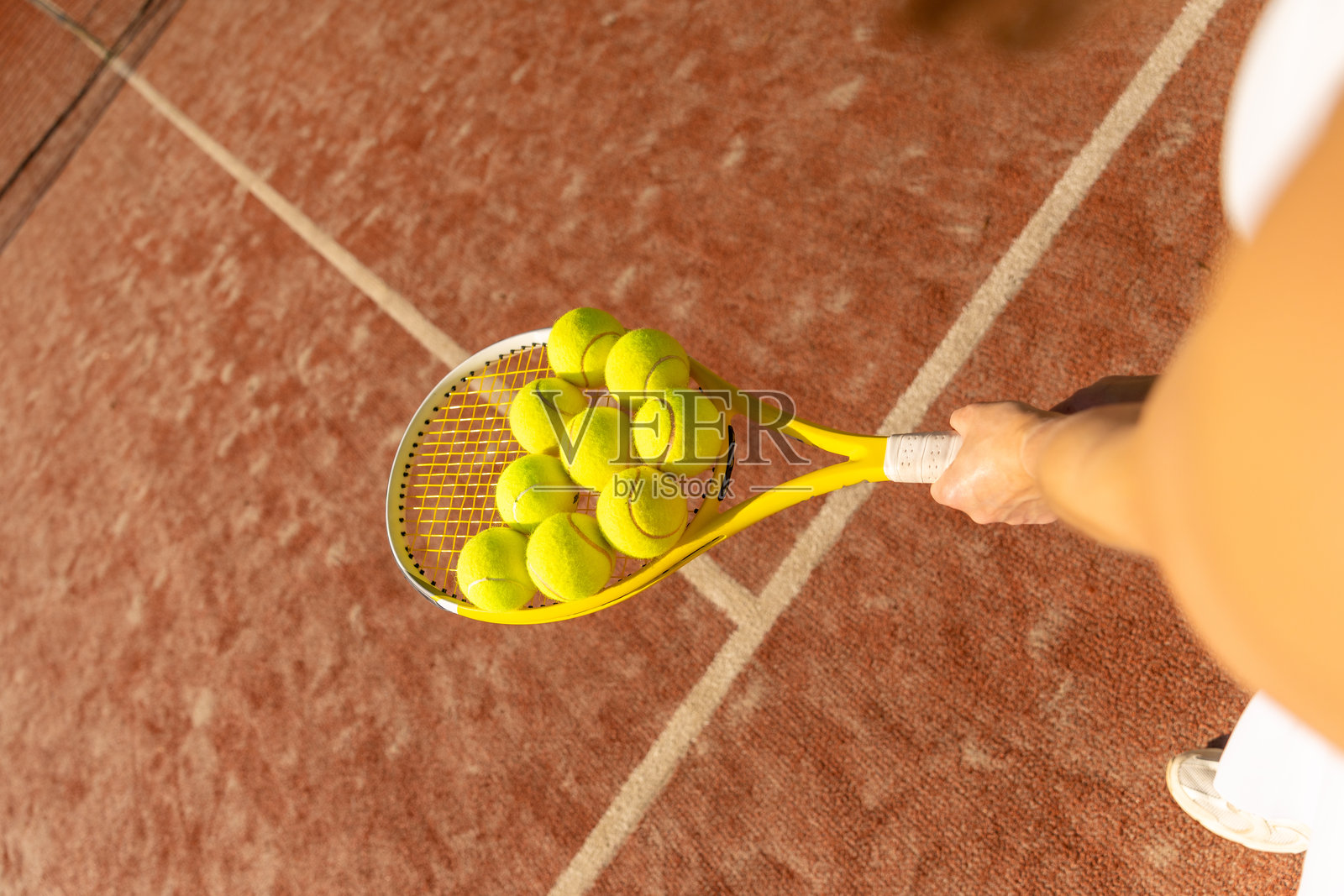 特写镜头：网球拍上放着多个黄色网球，背景是红土球场。照片摄影图片