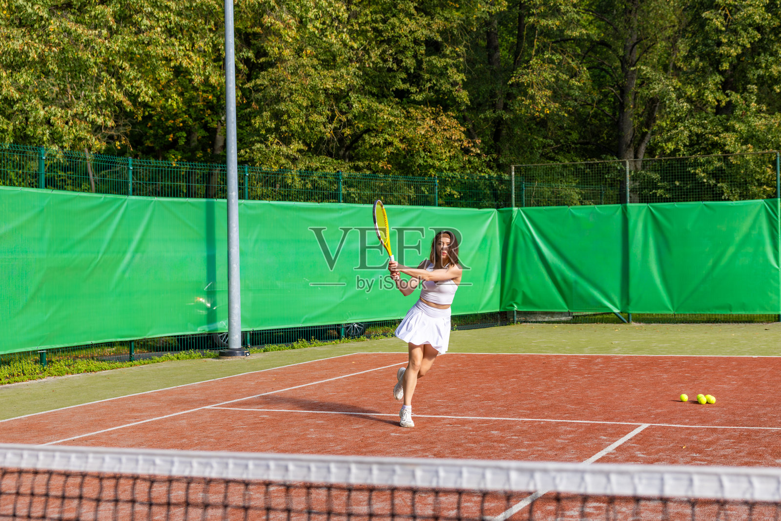 网球运动员在红土球场上向前跑动，准备用正手击球。照片摄影图片