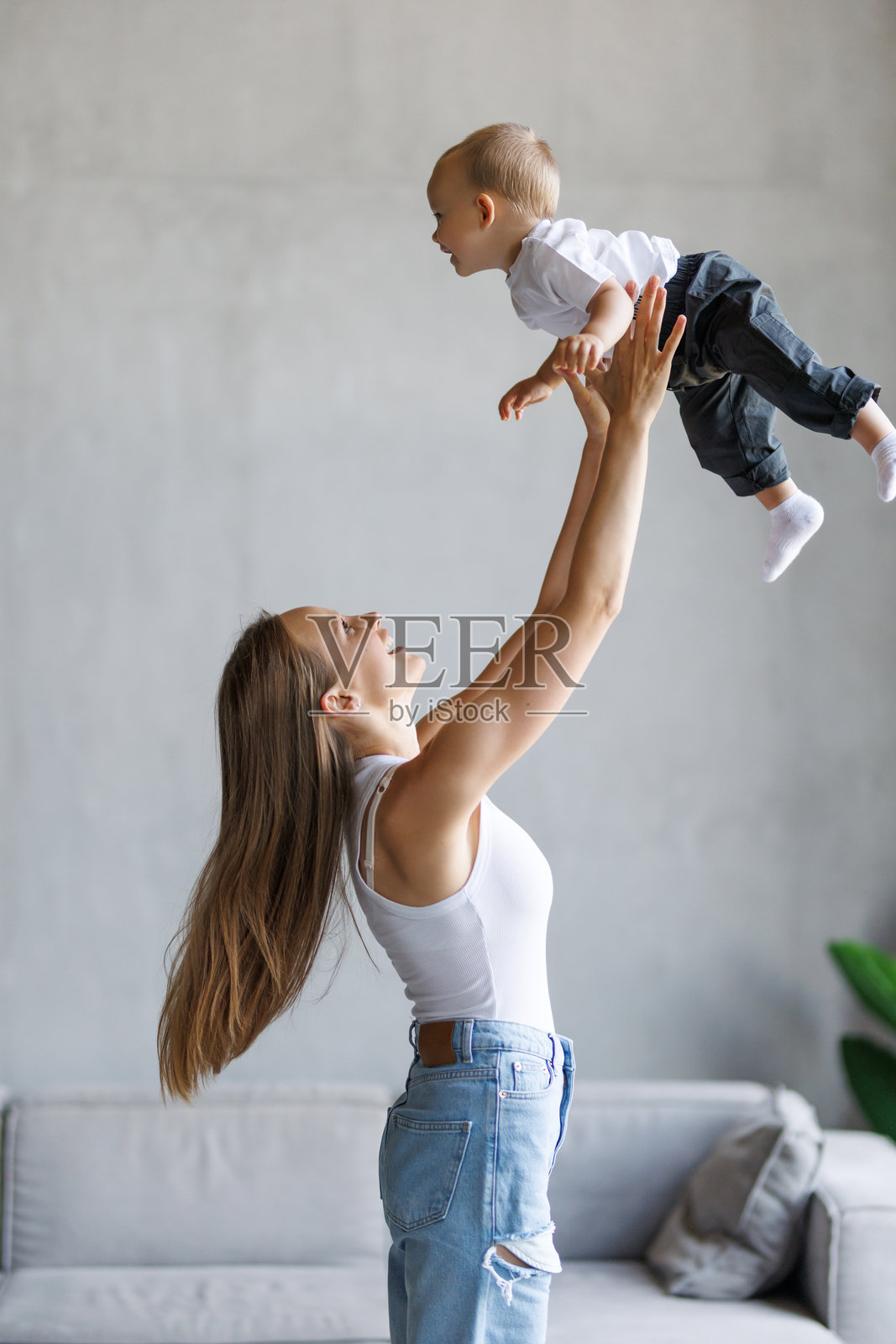 快乐的年轻母亲和可爱的蹒跚学步的儿子在家玩耍，抱着有趣的孩子假装飞翔，一起享受欢乐时光照片摄影图片