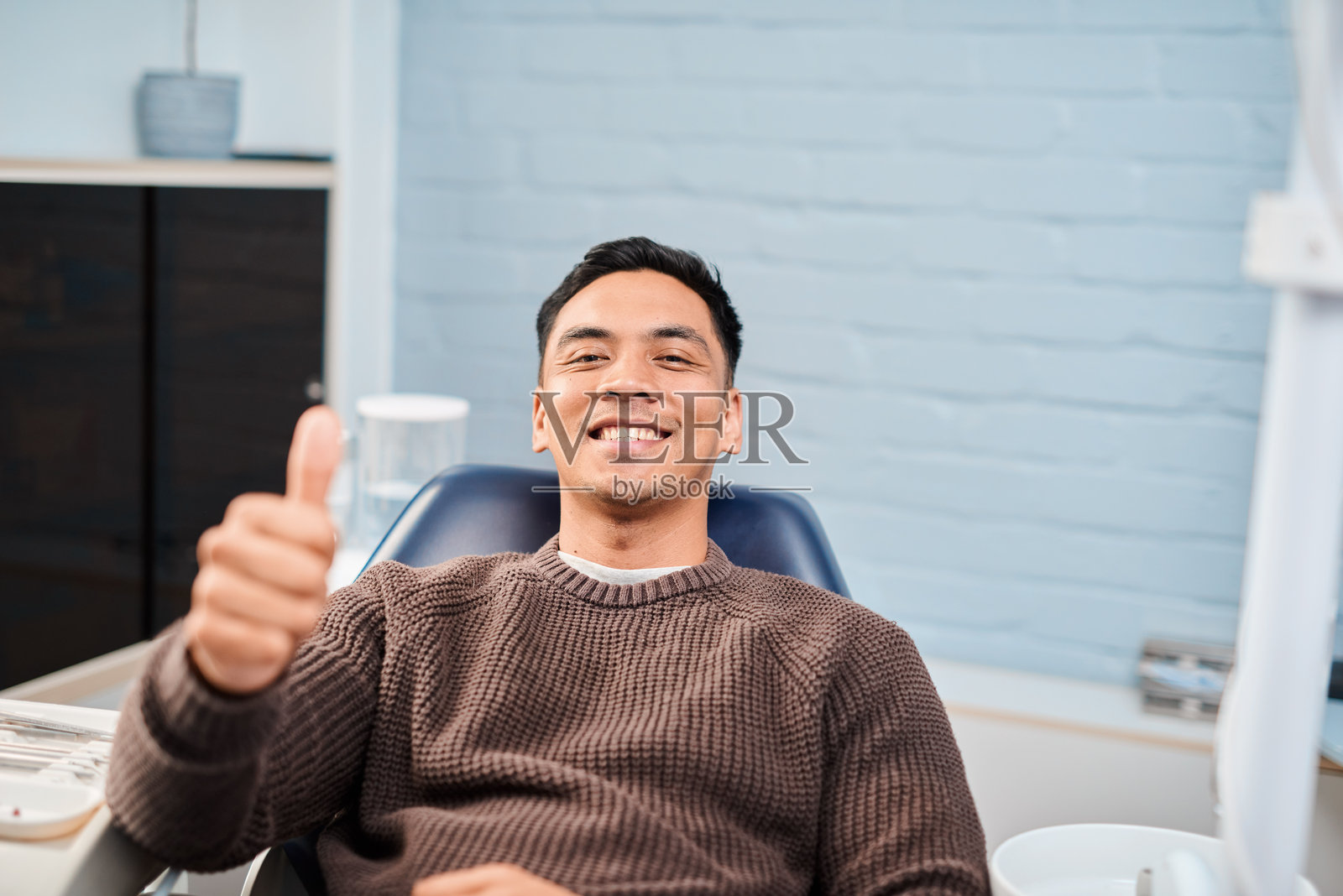 现代牙科诊所里，一名开心的患者坐在牙科椅上竖起大拇指。照片摄影图片