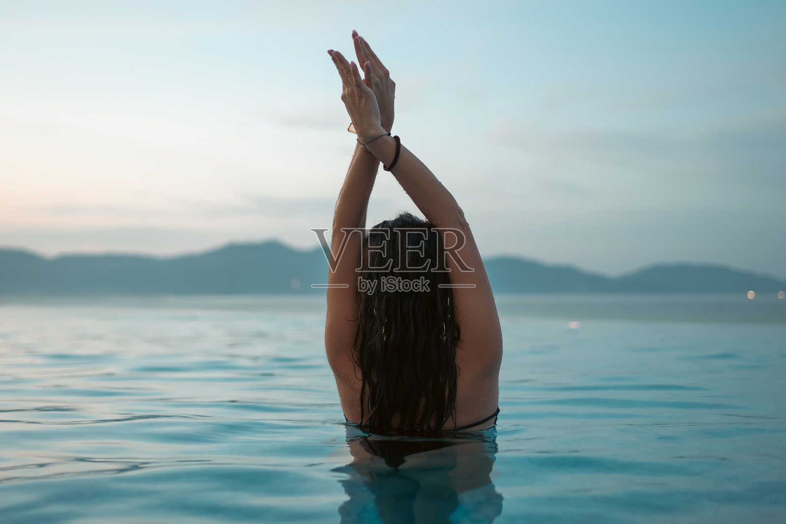 日落时分，美丽的女子在豪华泳池中畅游，泳池融入大海，尽显优雅假期与热带宁静，迷人的女子在日出时分于奢华度假村泳池中放松身心。照片摄影图片