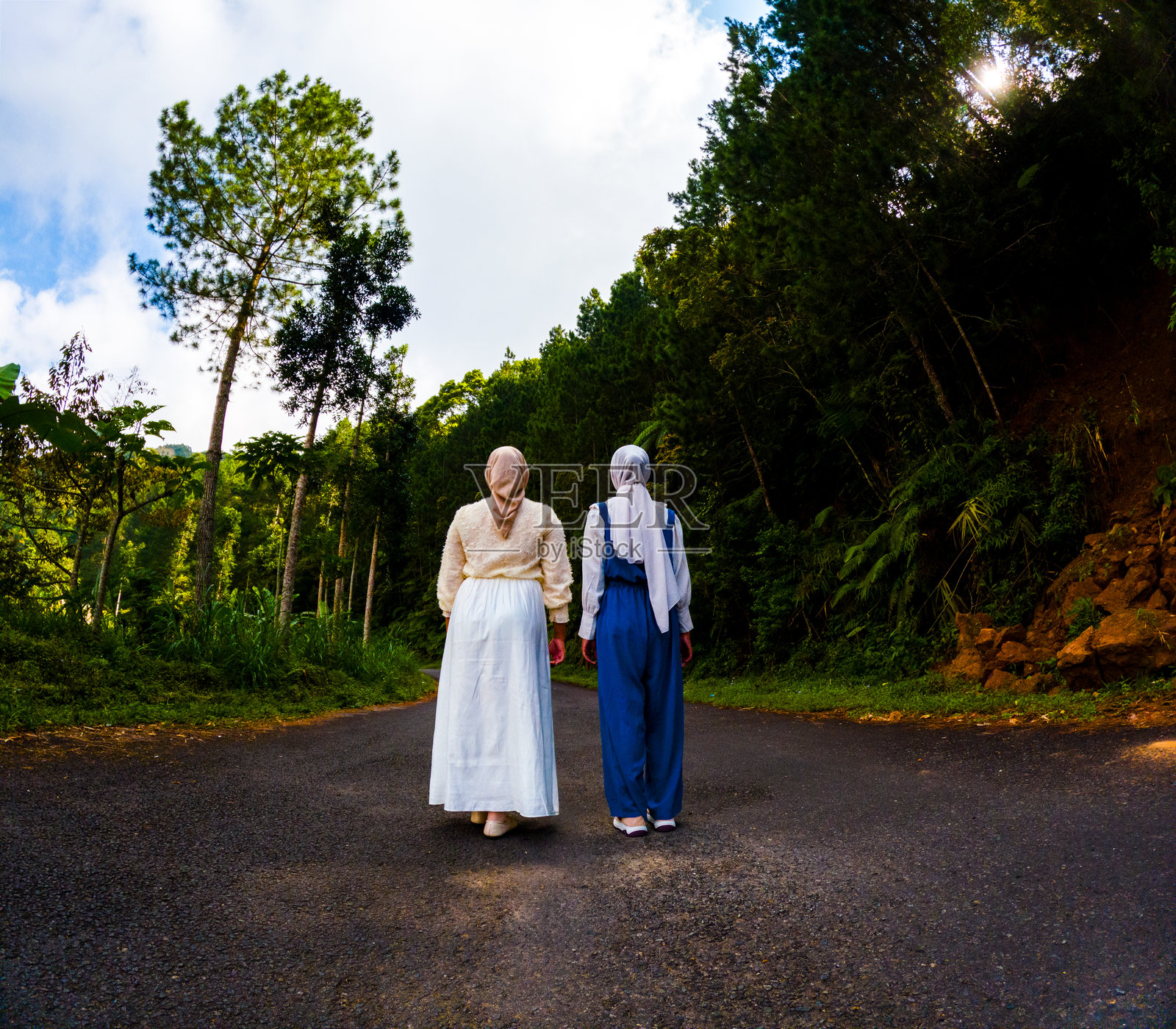 两位穆斯林亚洲女性走在一条宁静的高速公路上，周围是树林。森林浴。照片摄影图片