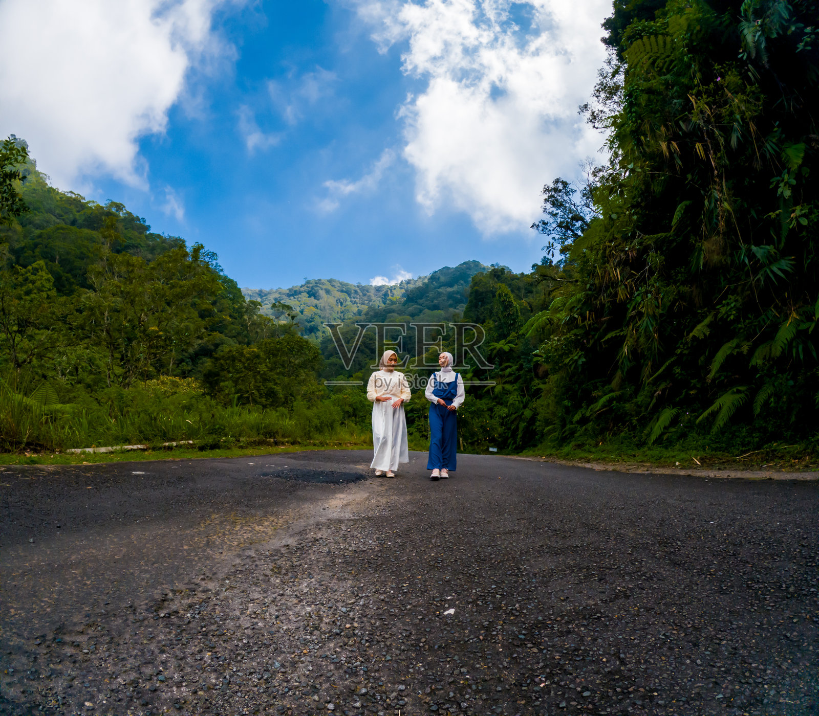 两位穆斯林亚洲女性走在一条宁静的高速公路上，道路两旁绿树成荫。森林浴。照片摄影图片