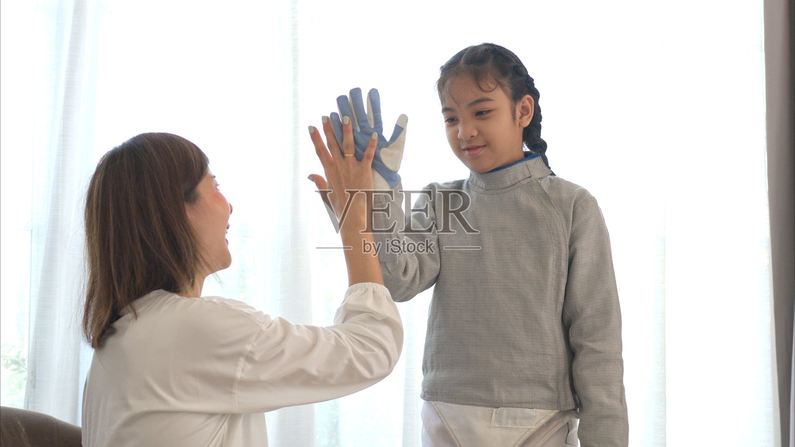 一名身穿击剑装备的女孩和她的母亲在备战即将到来的比赛日，正在为击剑练习做准备，整理体育器材。照片摄影图片