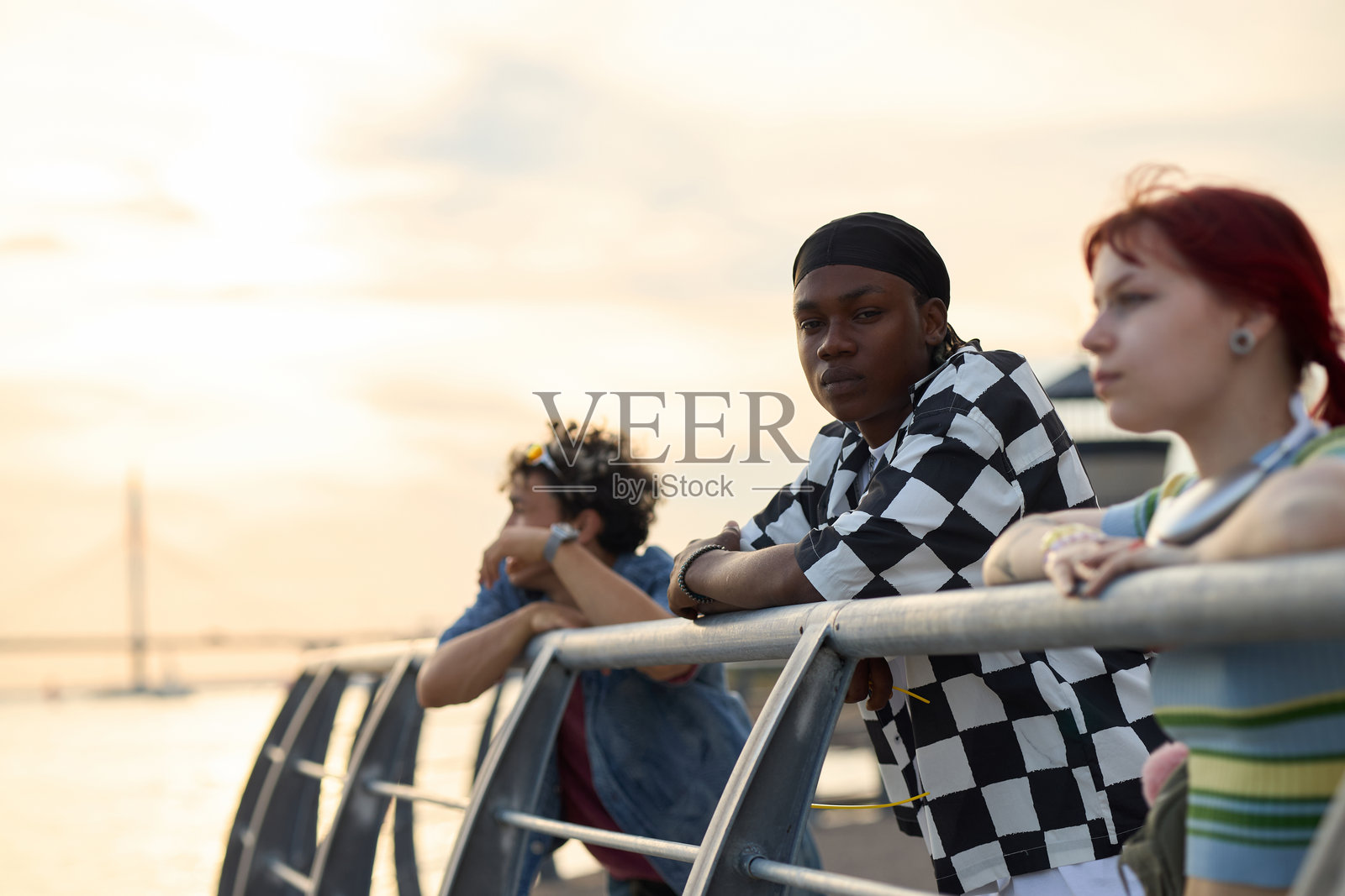 年轻的多民族朋友们靠在栏杆上，在户外欣赏日落照片摄影图片